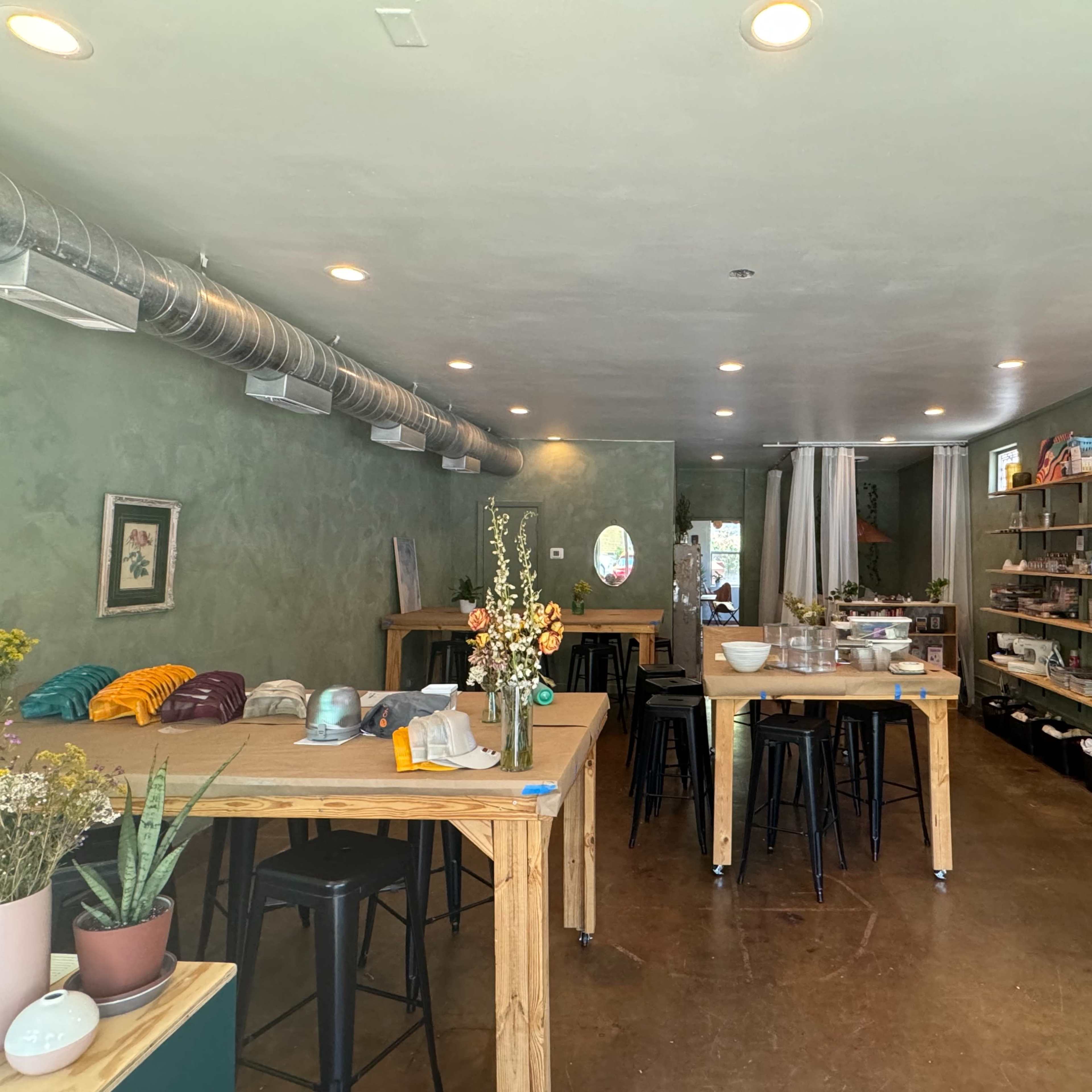 A spacious interior of a shop featuring wooden tables, shelves stocked with various items, and green walls.