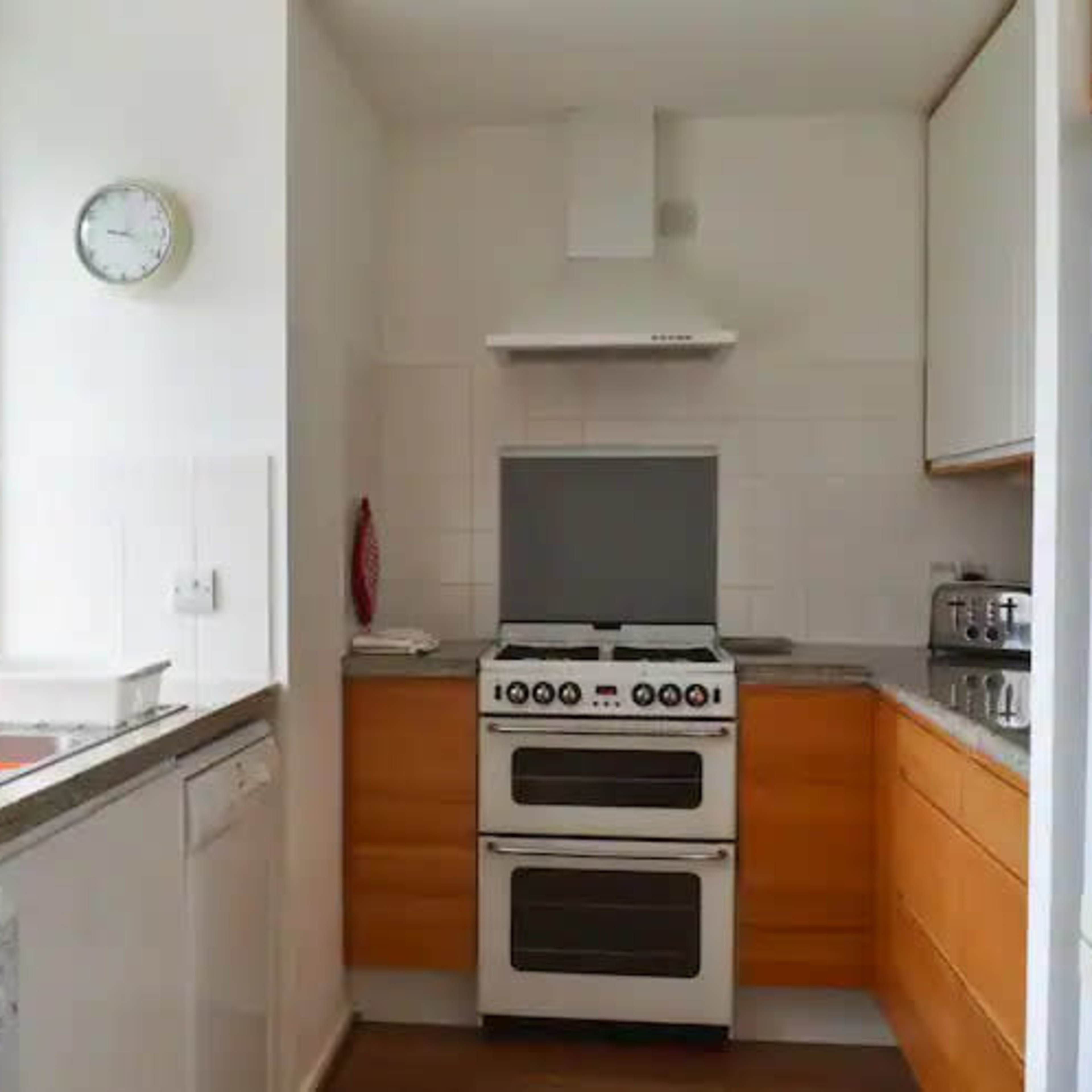 A compact kitchen features a stove, sink, and refrigerator against white walls and wooden cabinetry.