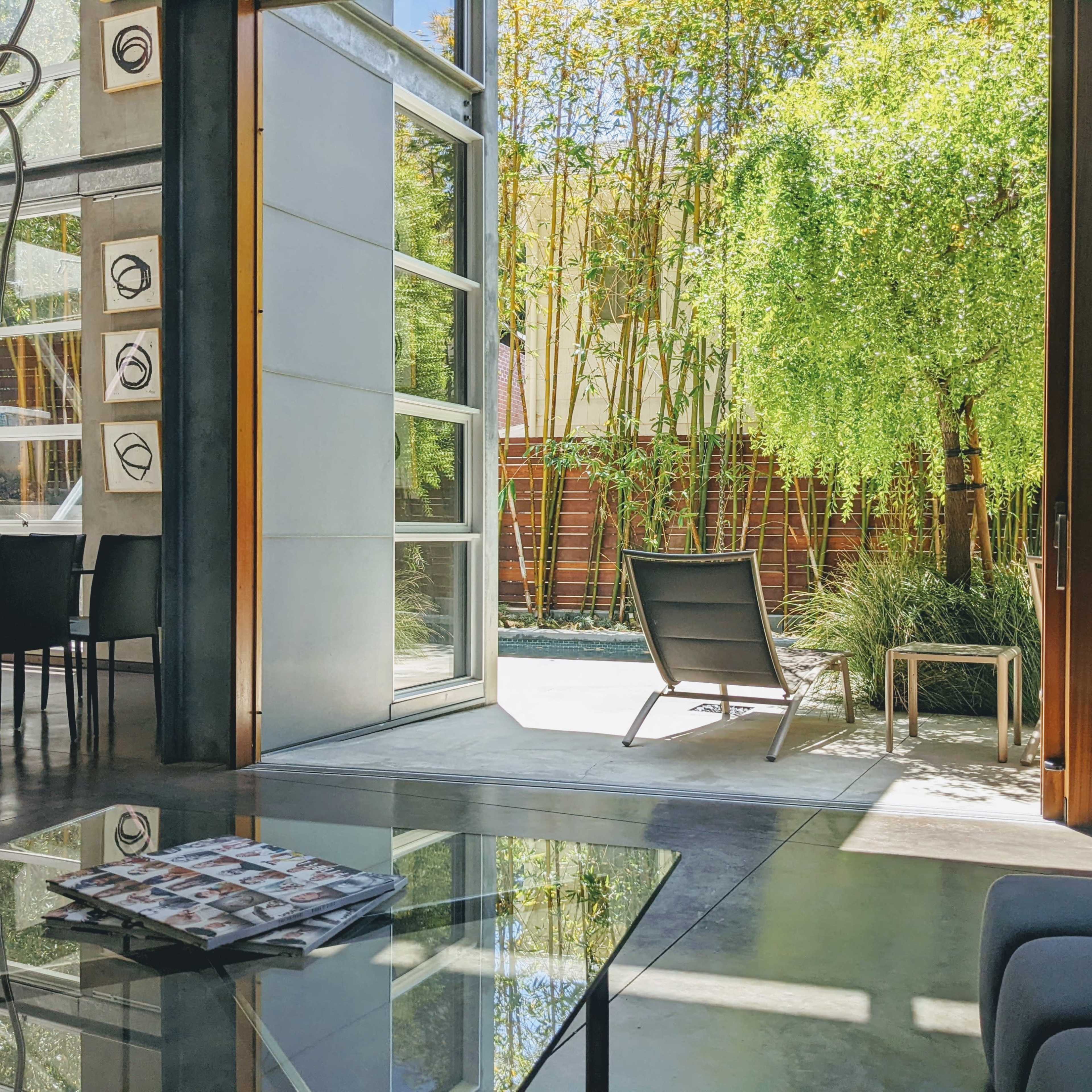 A modern living space features large glass doors opening to a serene outdoor area with bamboo and lounge chairs.