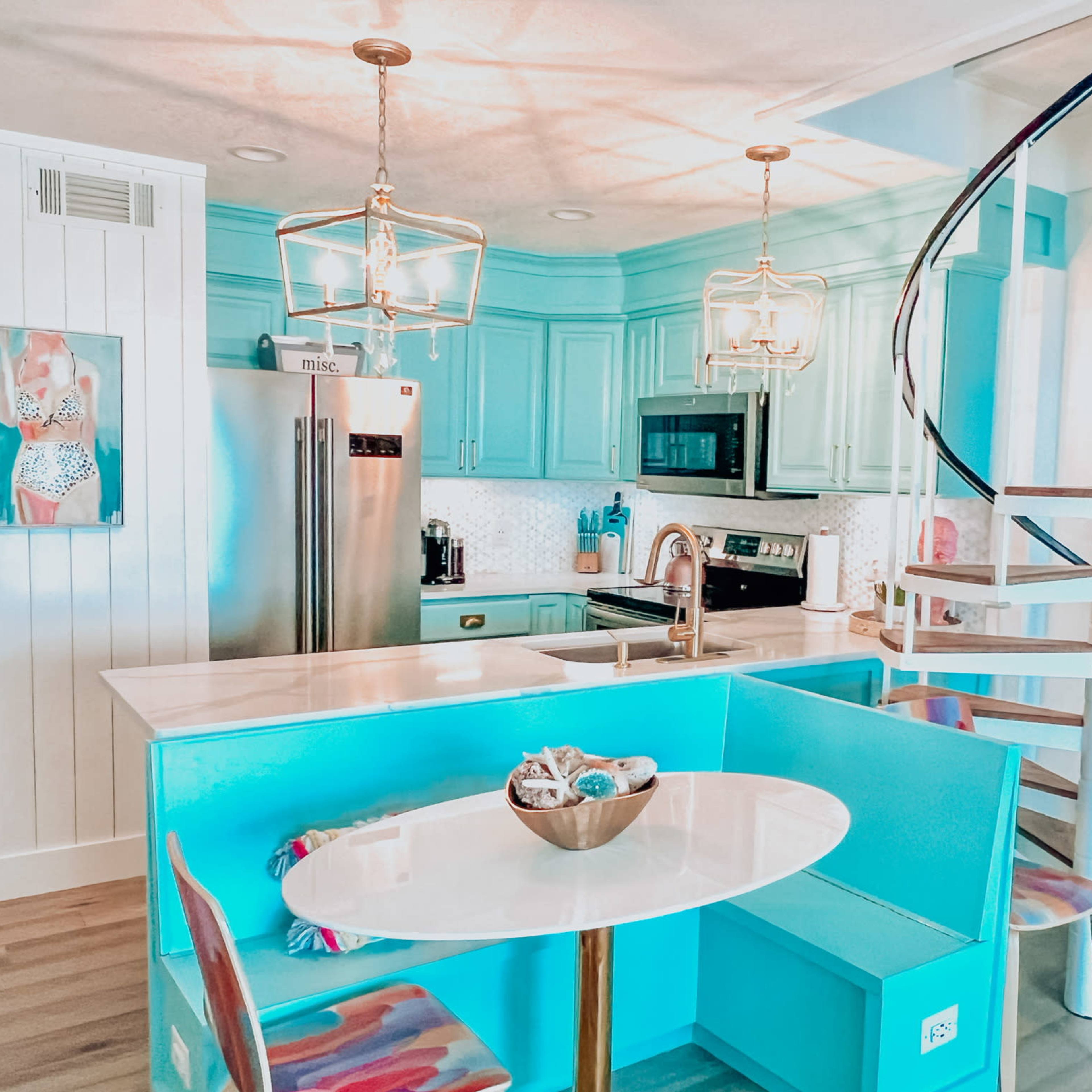 A modern kitchen with turquoise cabinets, a round dining table, and a spiral staircase leading to an upper level.