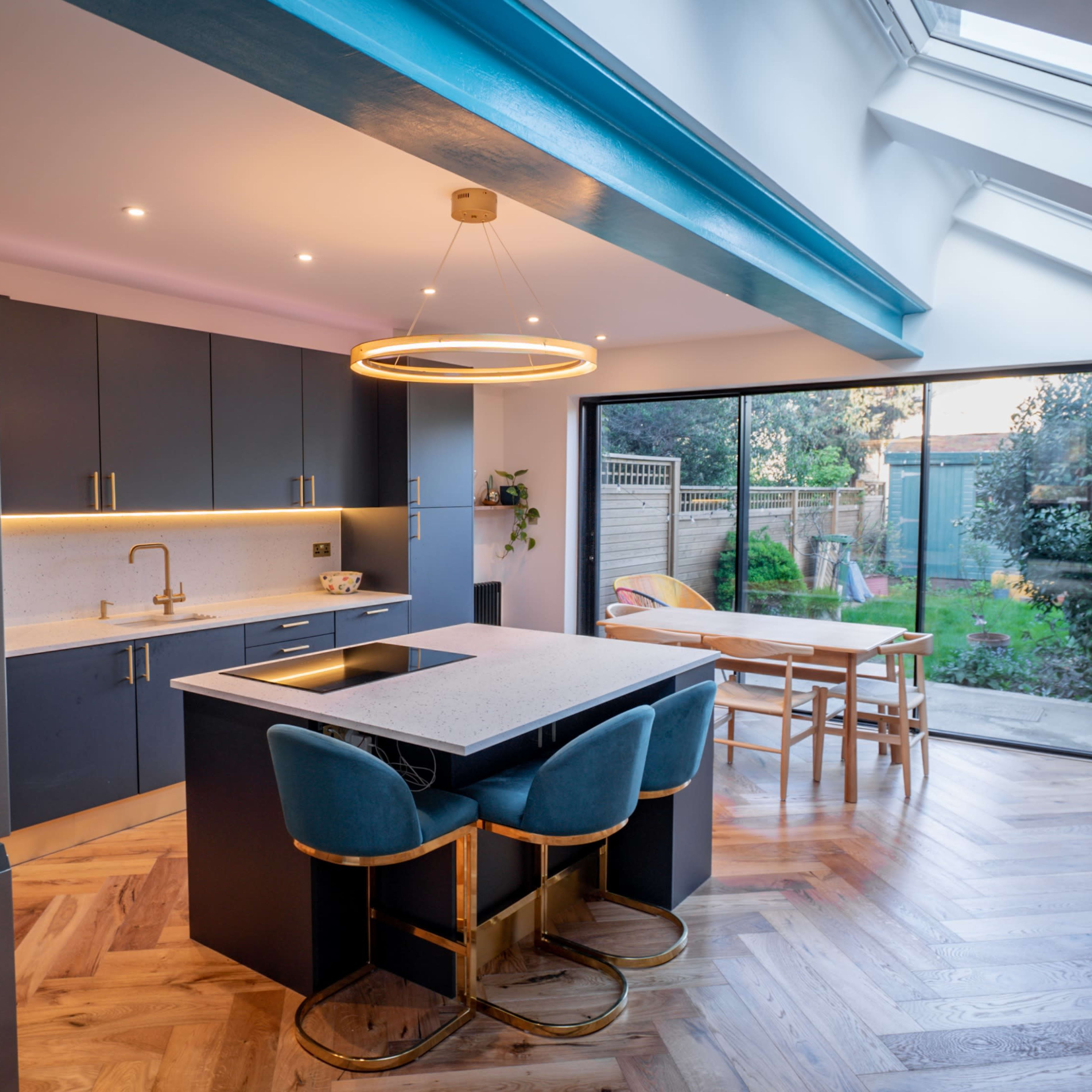 A modern kitchen features gray cabinetry, a central island with a sink, and large glass doors opening to a garden.