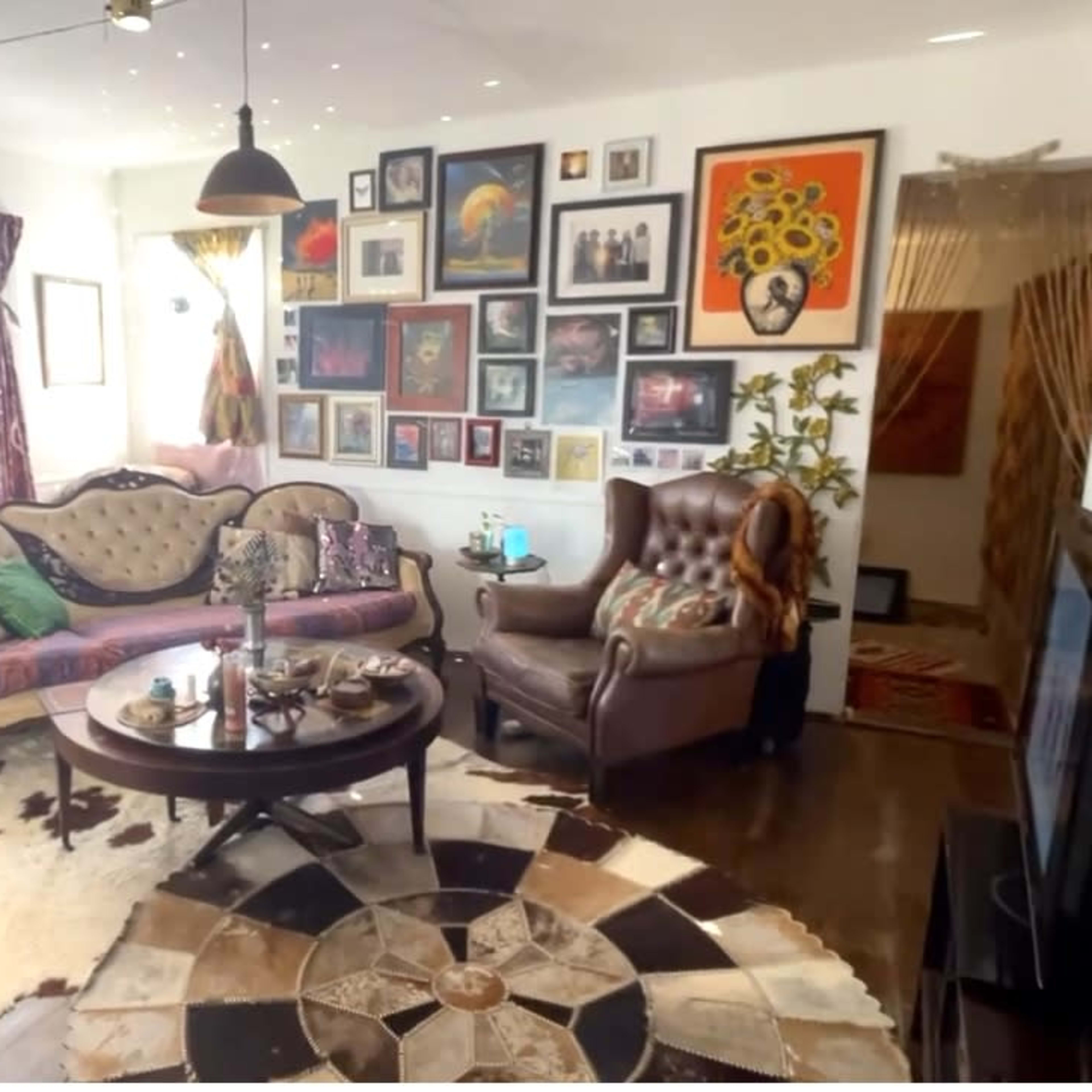 The room features a cozy seating area with a patterned rug, a round coffee table, and walls adorned with various framed artworks.