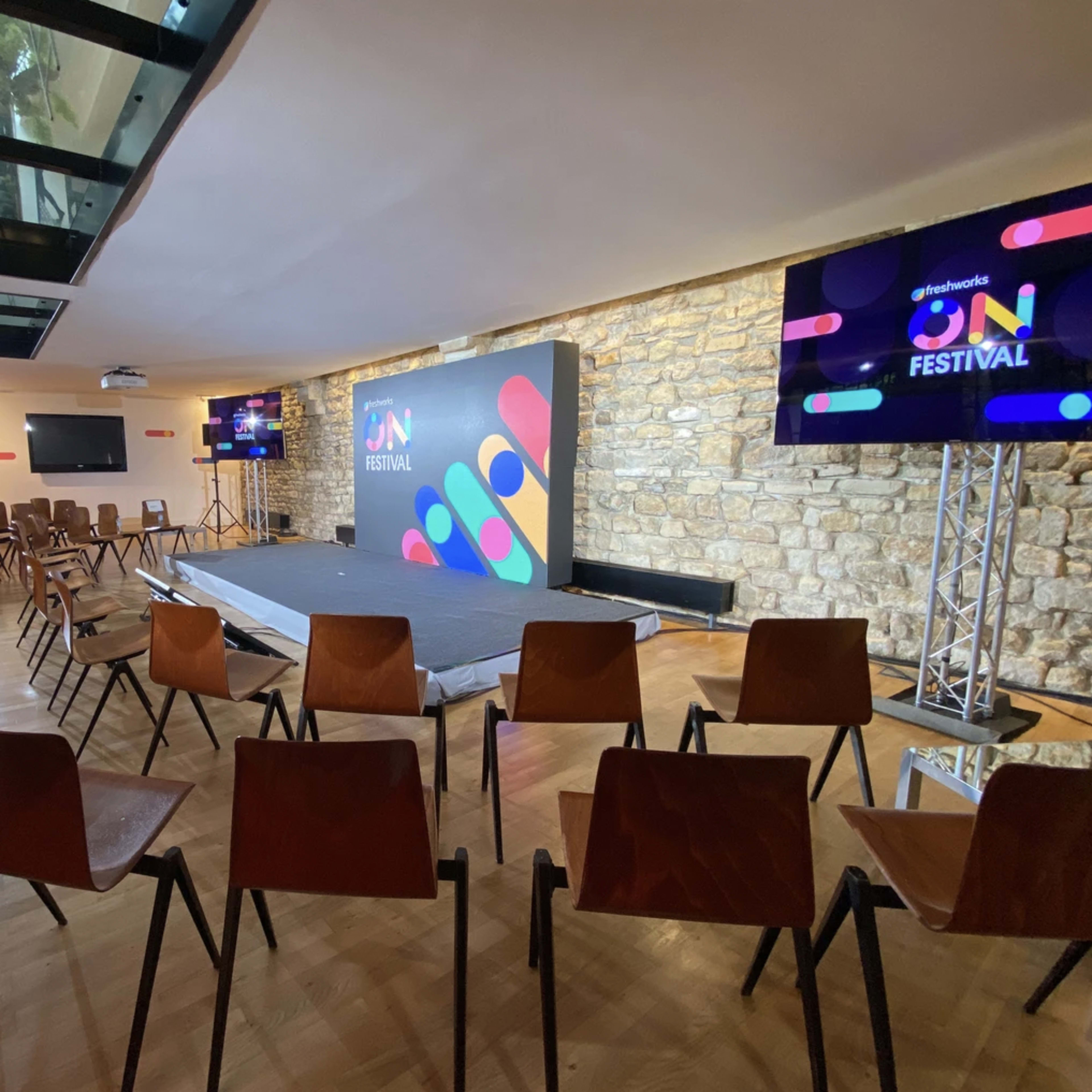 A stage is set up in a room with stone walls, surrounded by rows of wooden chairs arranged for an event.