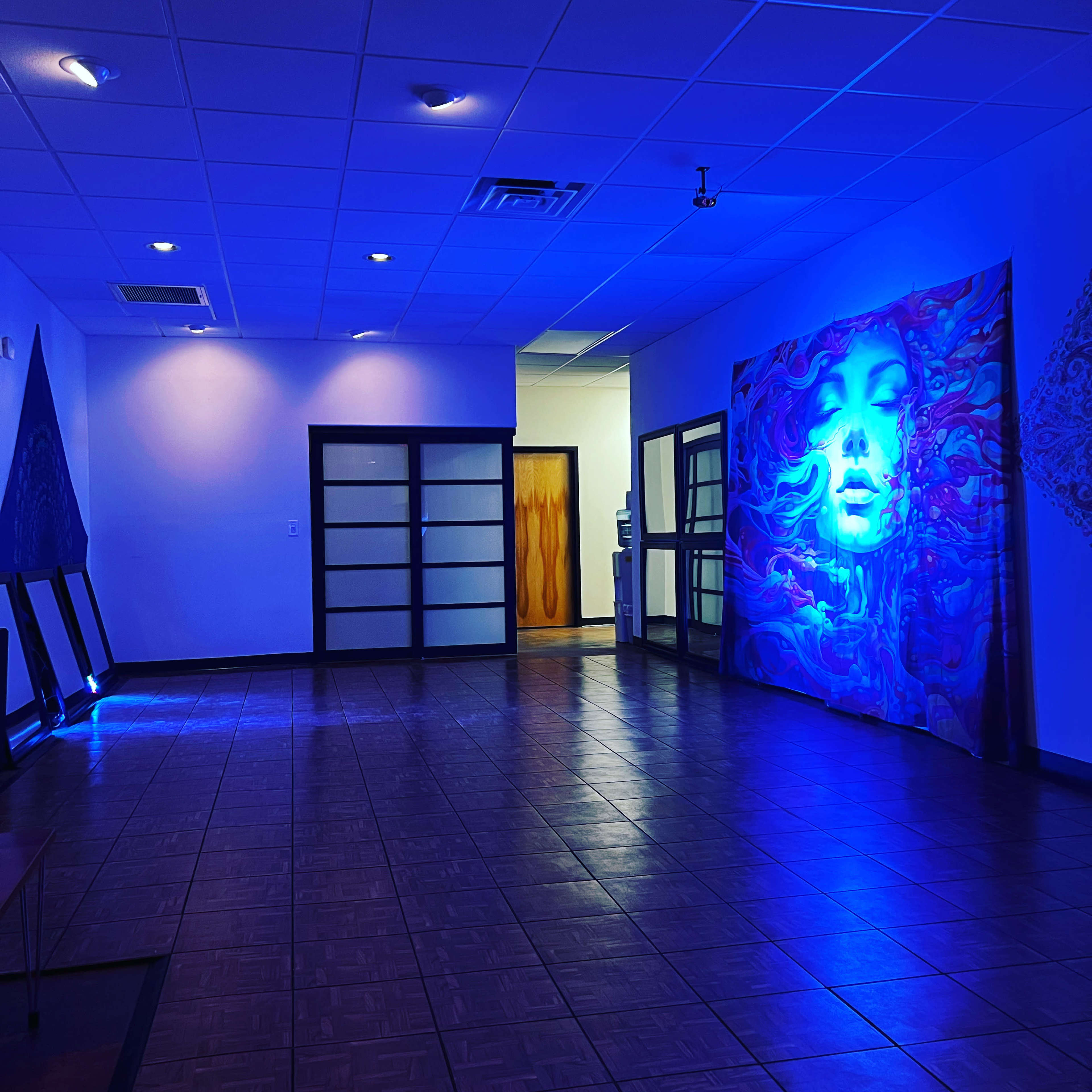 A spacious room with blue lighting features a large mural of a woman's face and two abstract art pieces leaning against the wall.