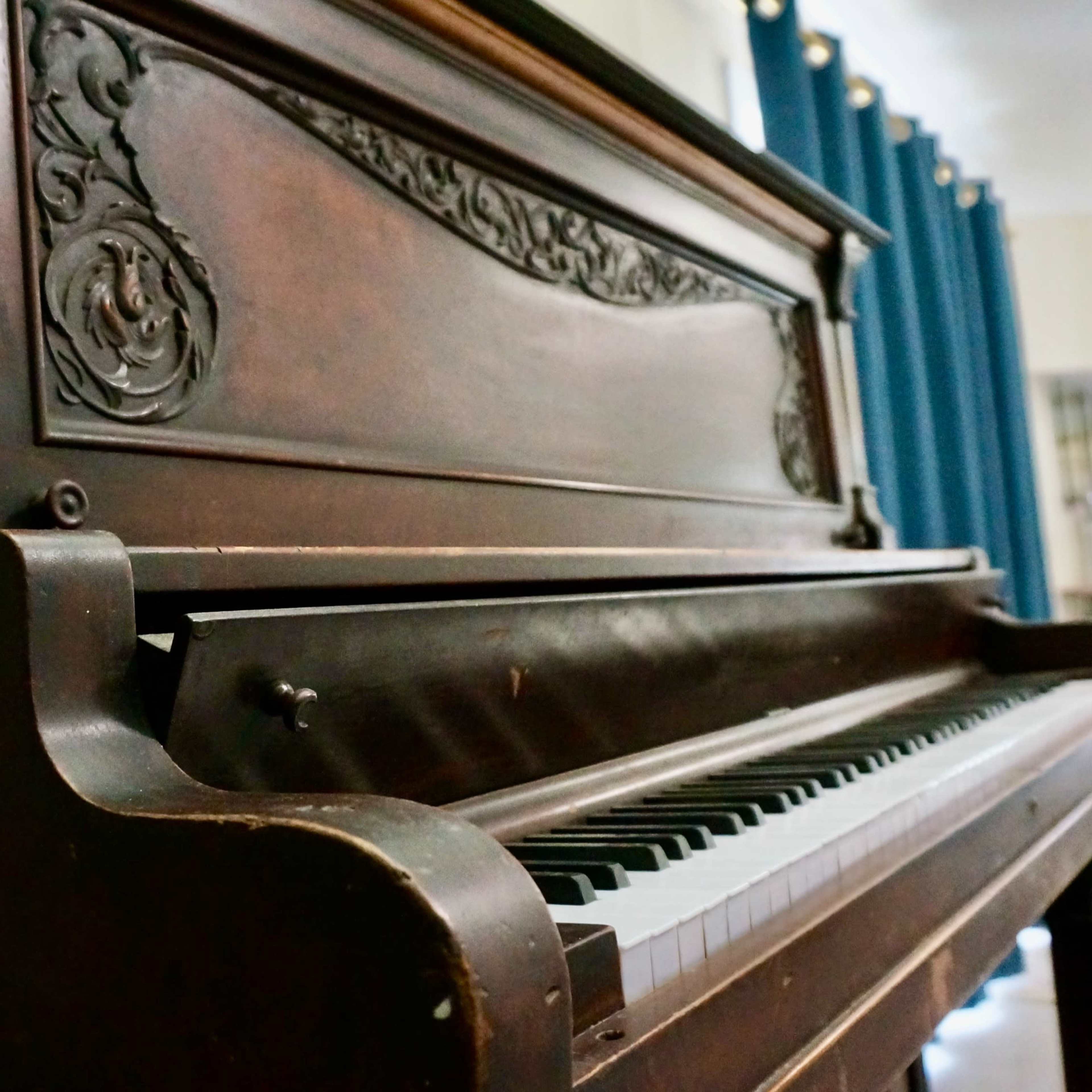 A close-up view of a vintage upright piano with intricate woodwork and a partially opened keyboard.