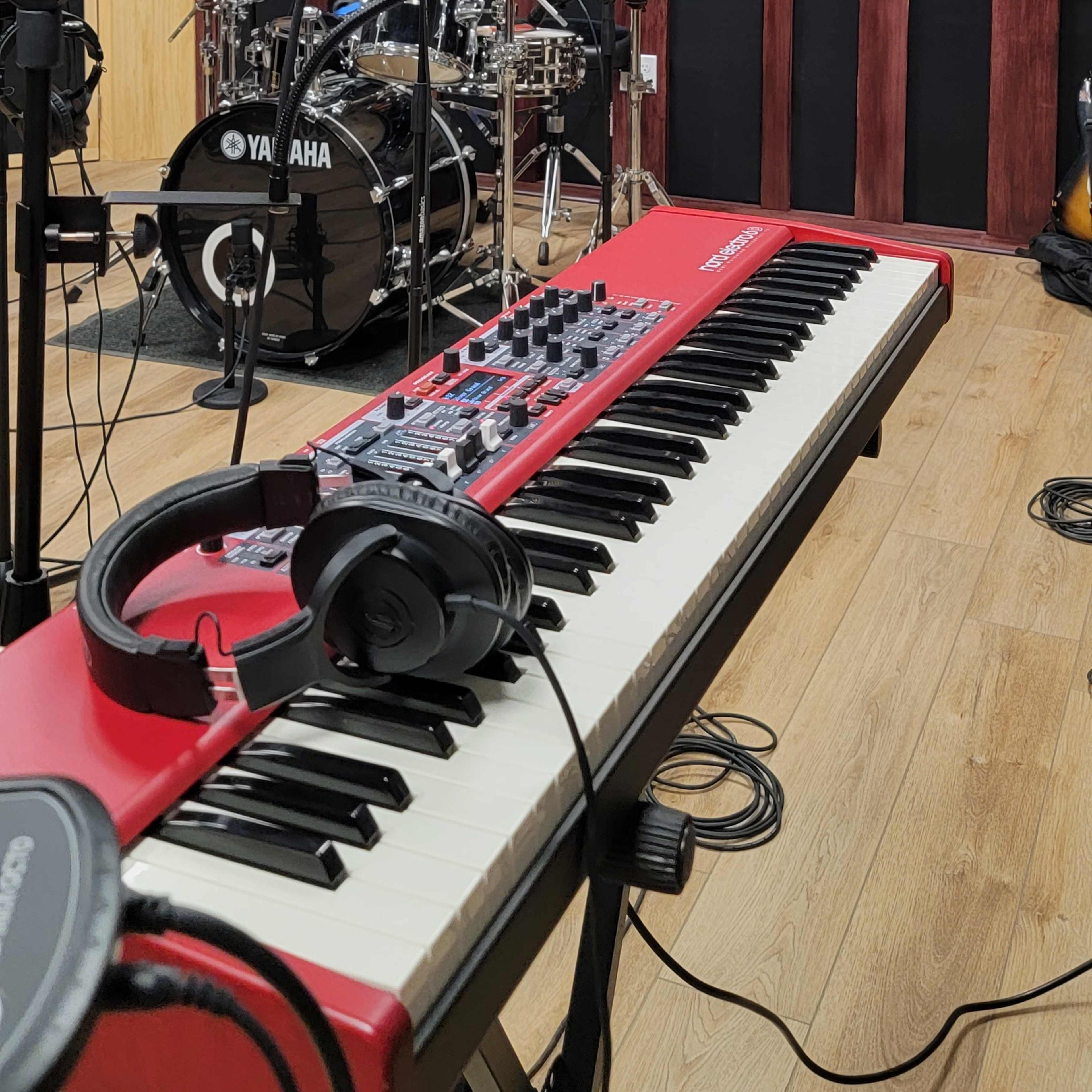 A music studio with a red keyboard, microphone, and a drum set arranged against a textured wall featuring wooden sound panels.