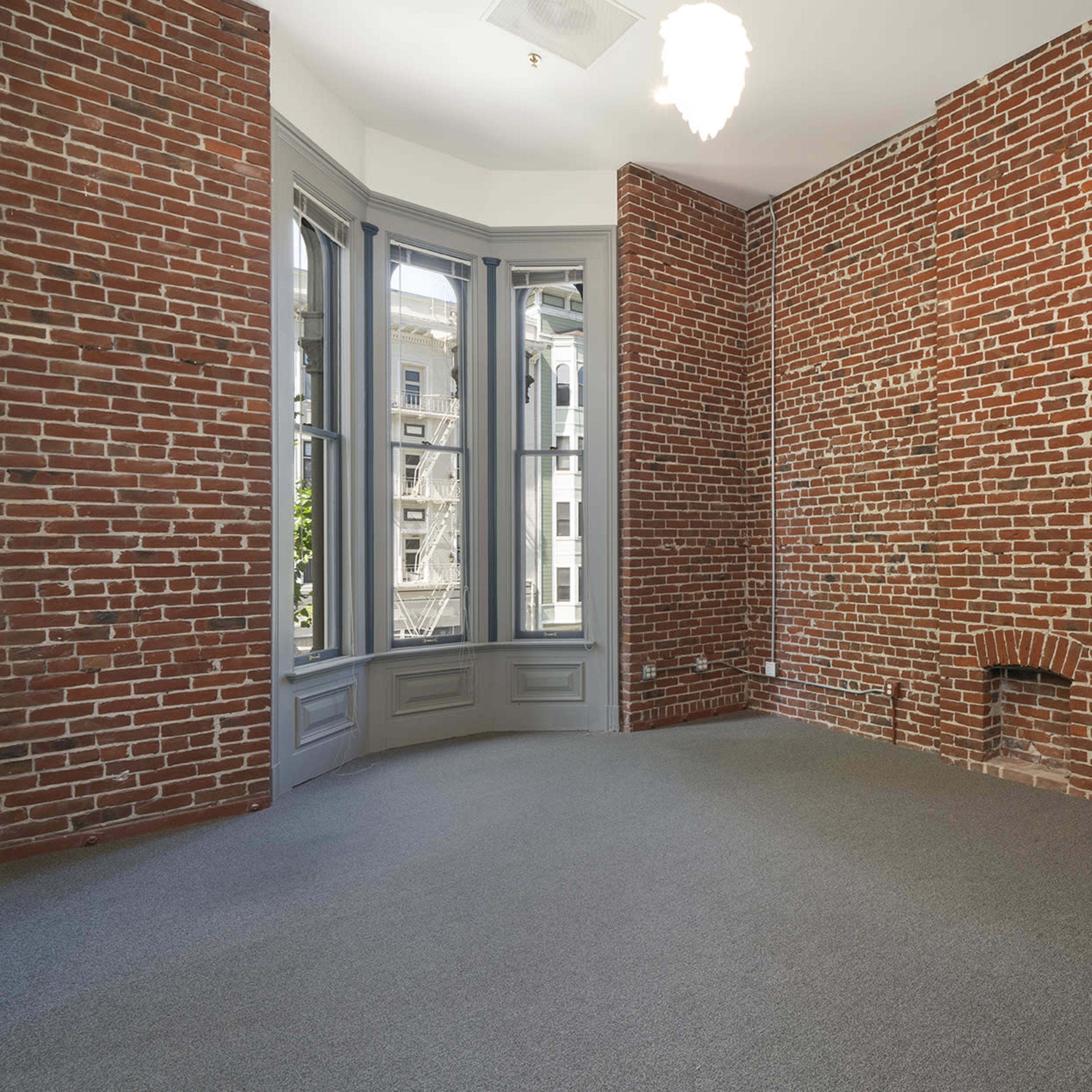 A room featuring exposed brick walls, a bay window, and a staircase leading to a loft area.
