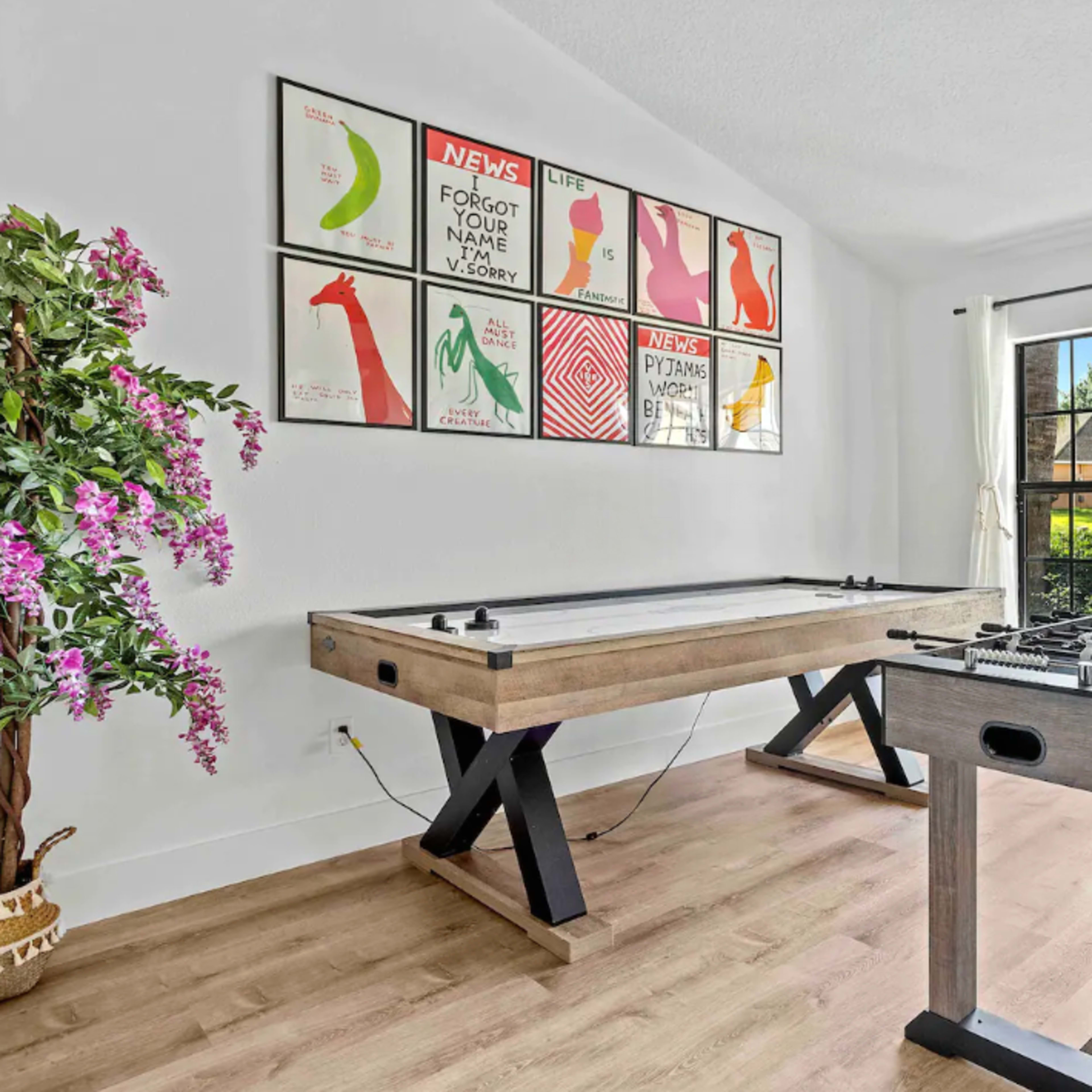 A bright room features a foosball table and an air hockey table against a wall adorned with colorful artwork.