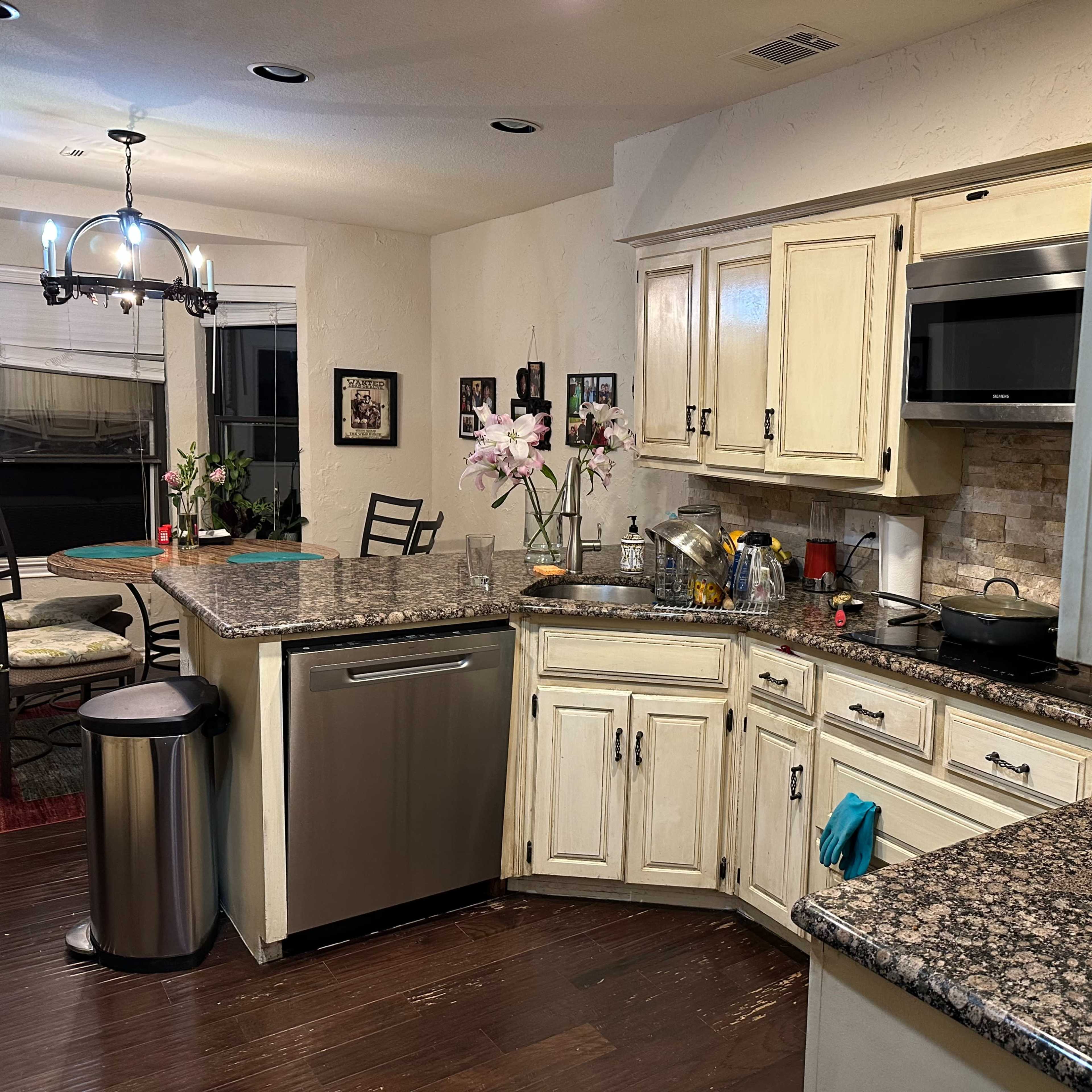 A corner kitchen features granite countertops, stainless steel appliances, and wooden cabinetry, with a dining area visible in the background.