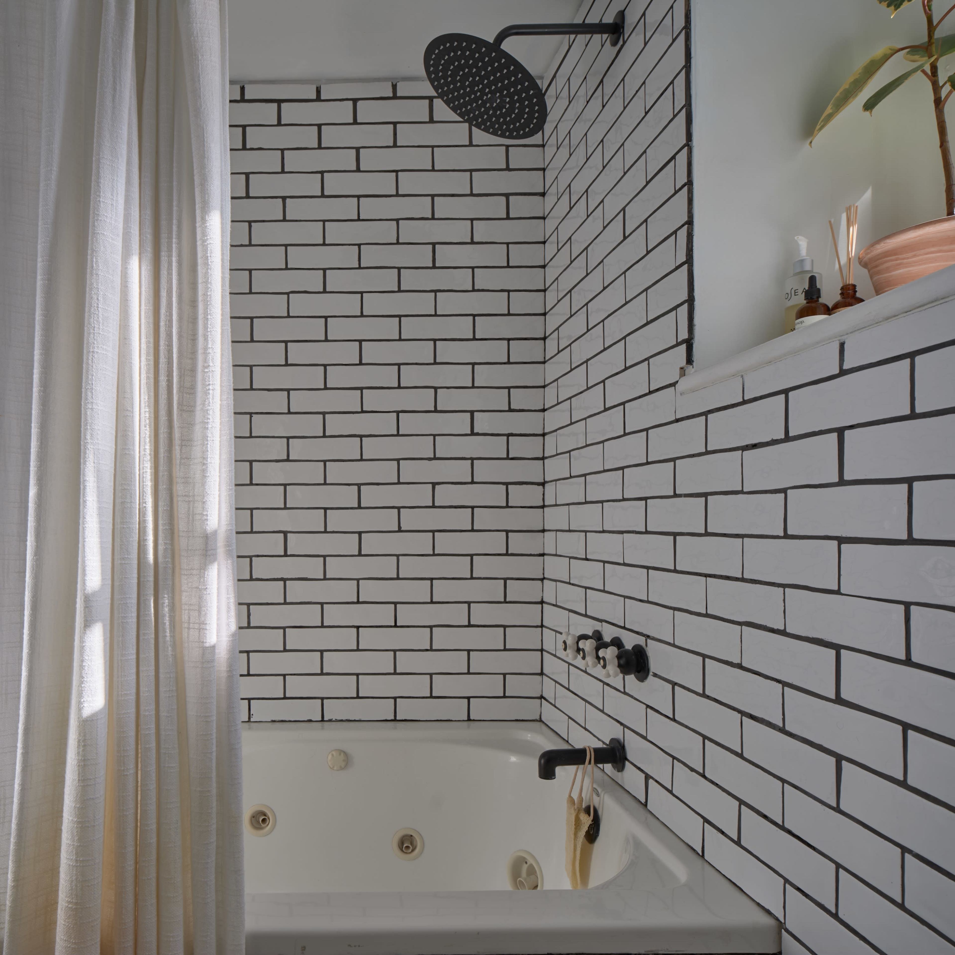 A modern bathroom featuring a white tiled wall with a showerhead, a bathtub, and a shower curtain.
