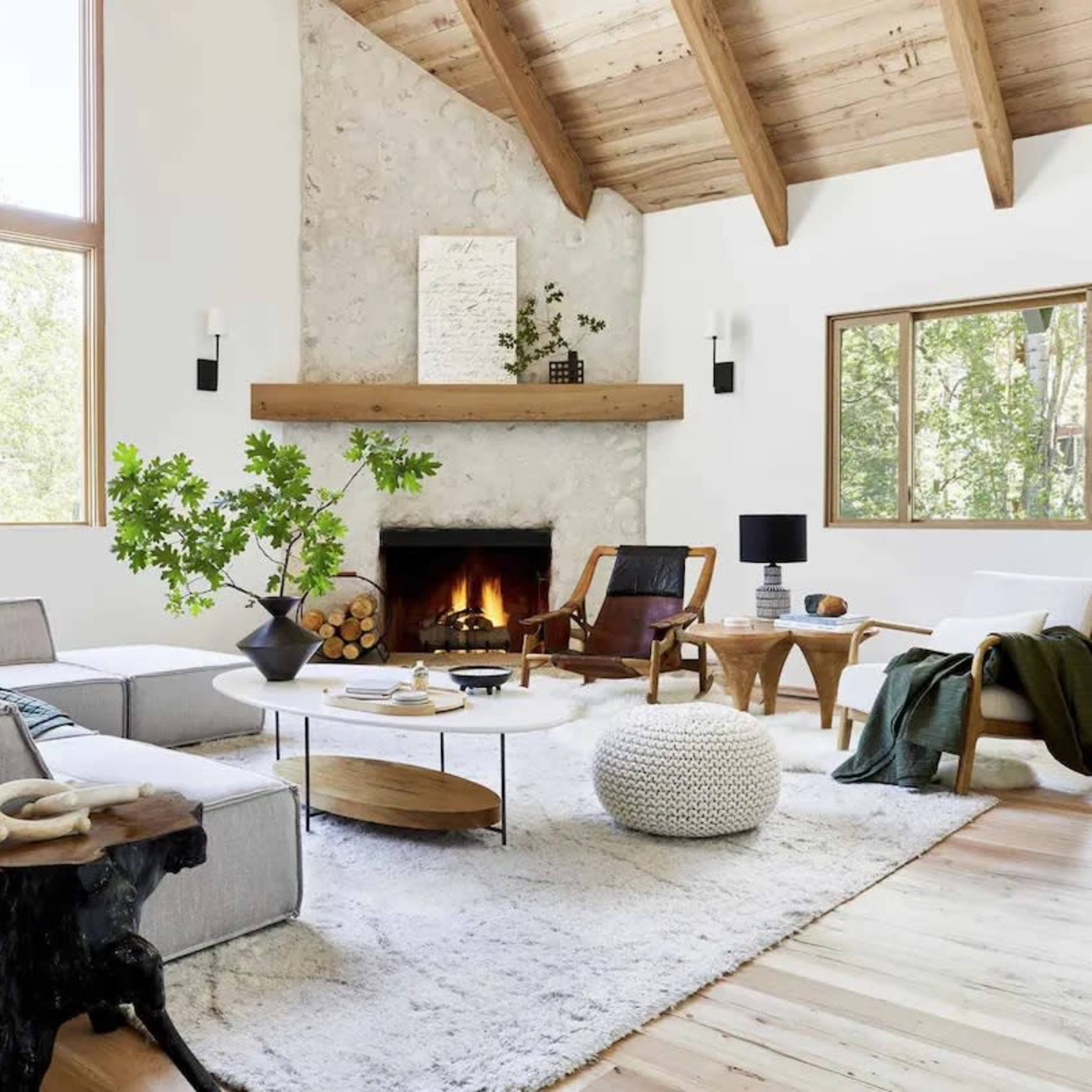 A spacious living room with a stone fireplace, large windows, and a mix of modern and rustic furniture.