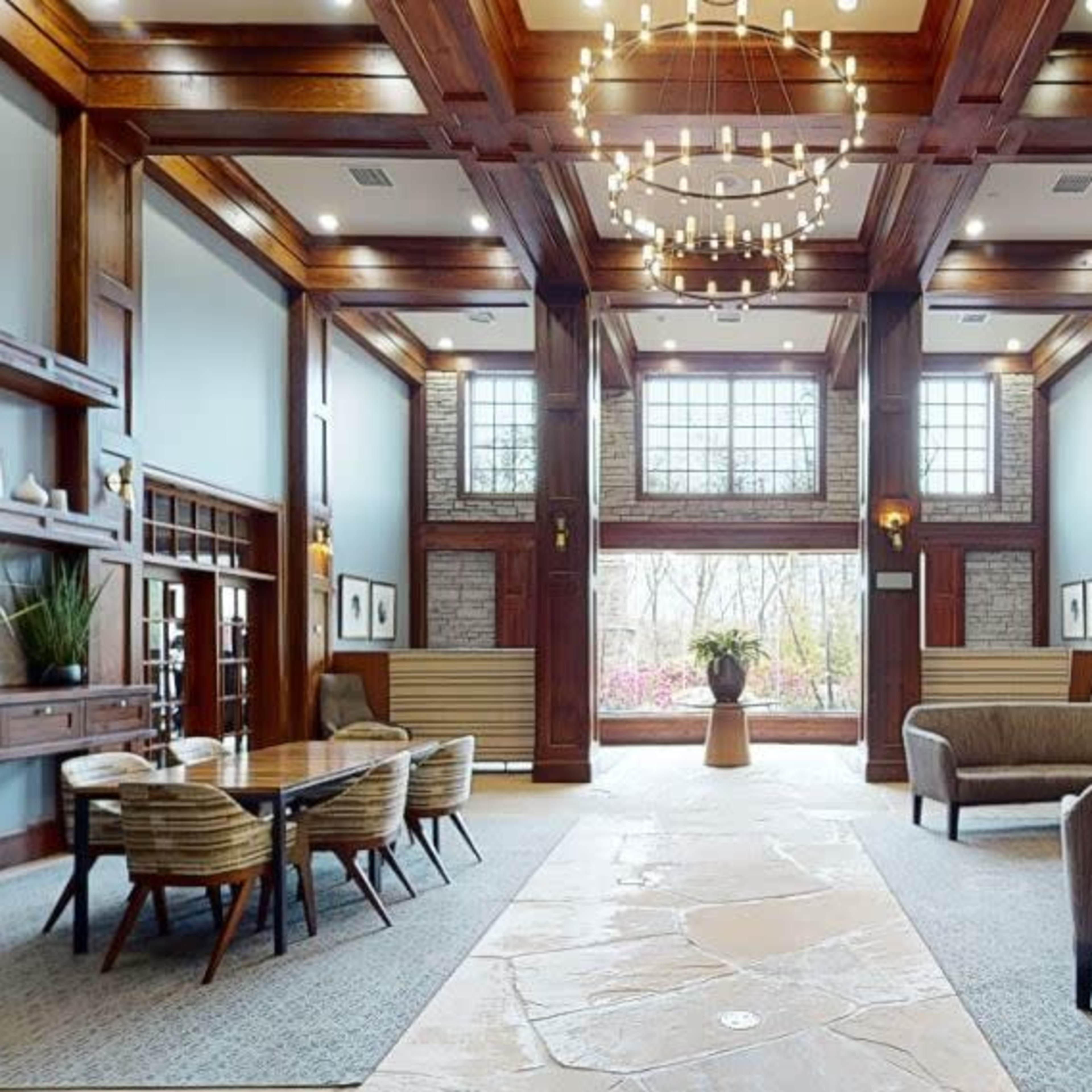 A spacious lobby interior featuring wooden pillars, a stone fireplace, modern seating arrangements, and large windows allowing natural light to fill the space.