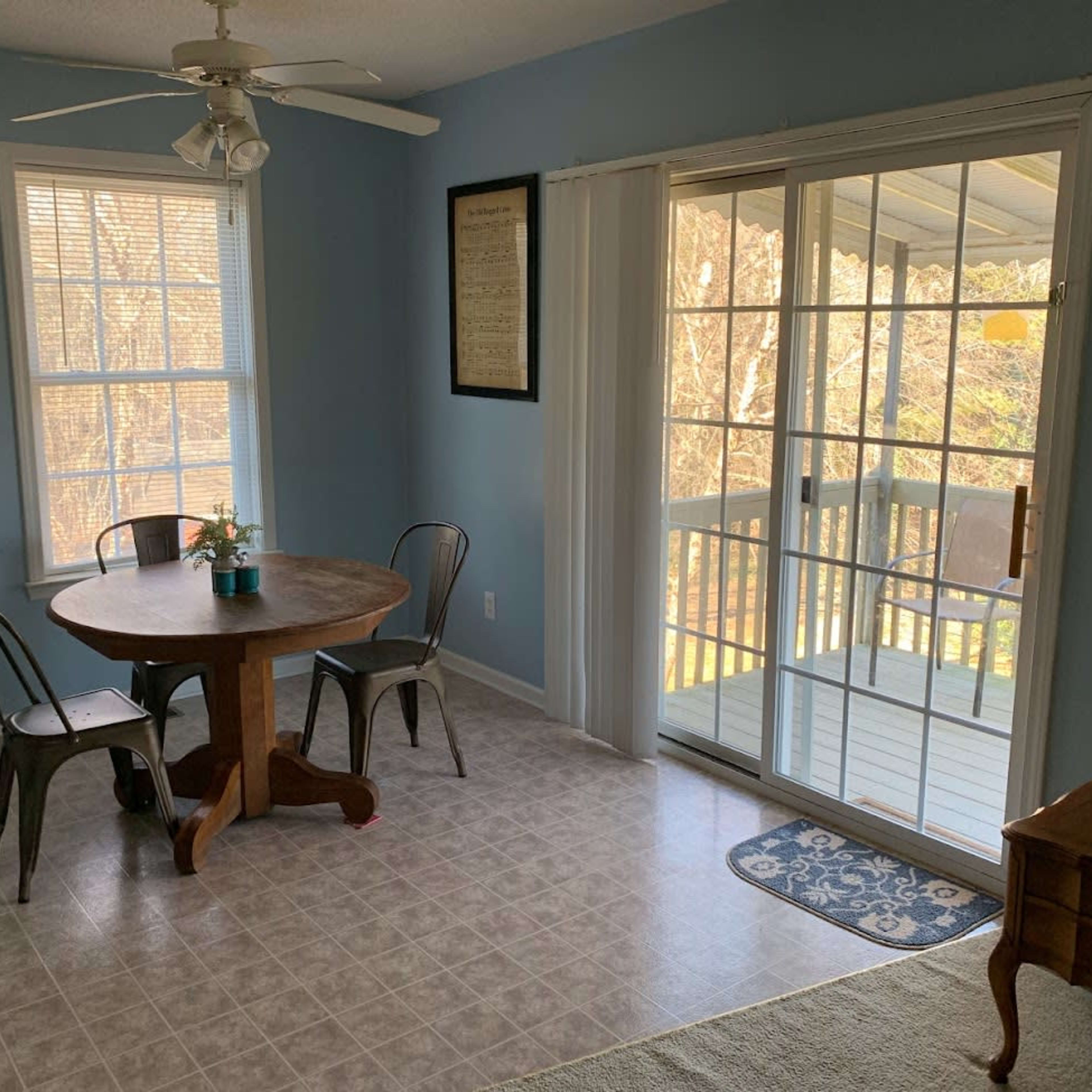 A dining area features a round wooden table with metal chairs, and sliding glass doors lead to an outdoor balcony.