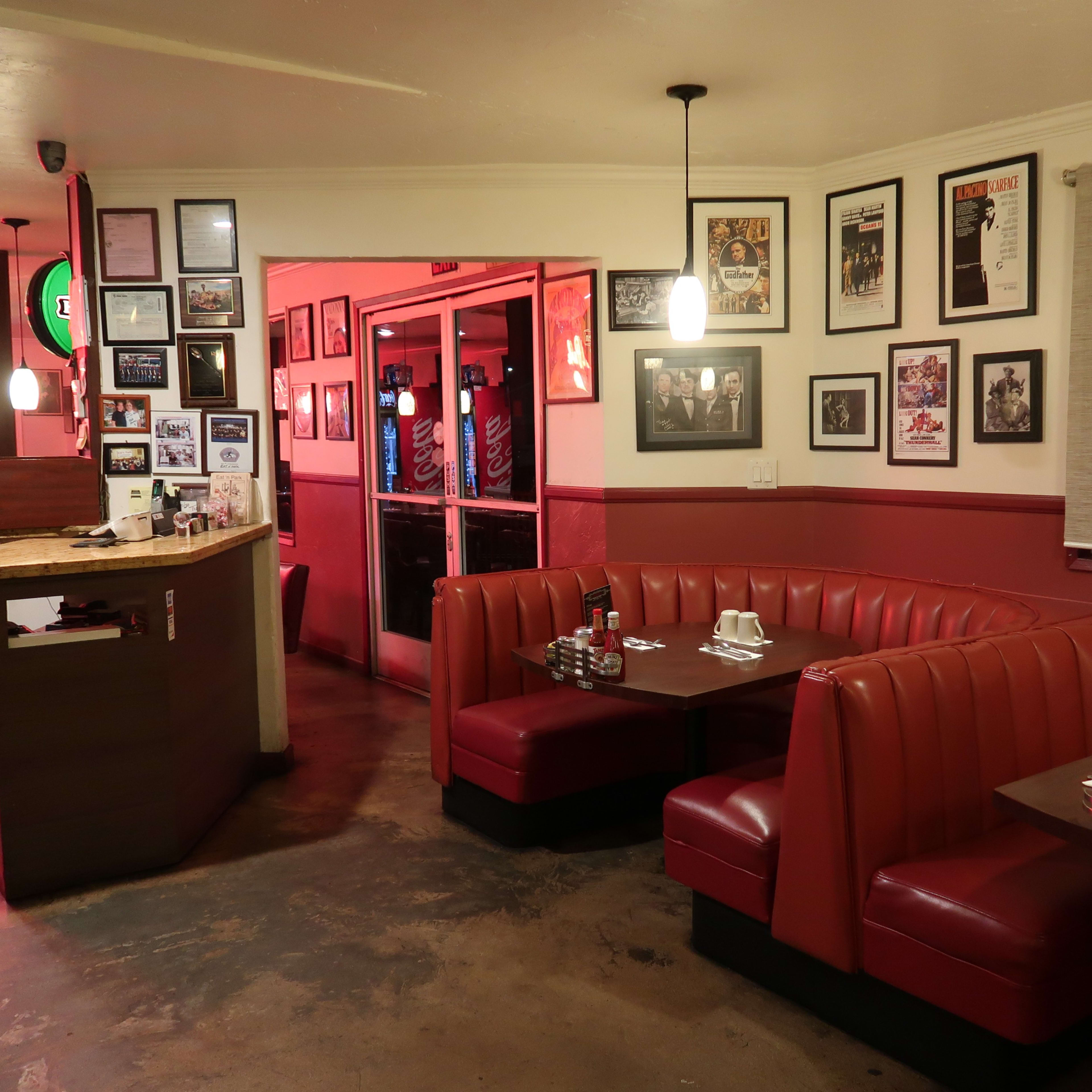 A diner interior featuring red booths, a food service counter, and walls adorned with framed photographs and posters.