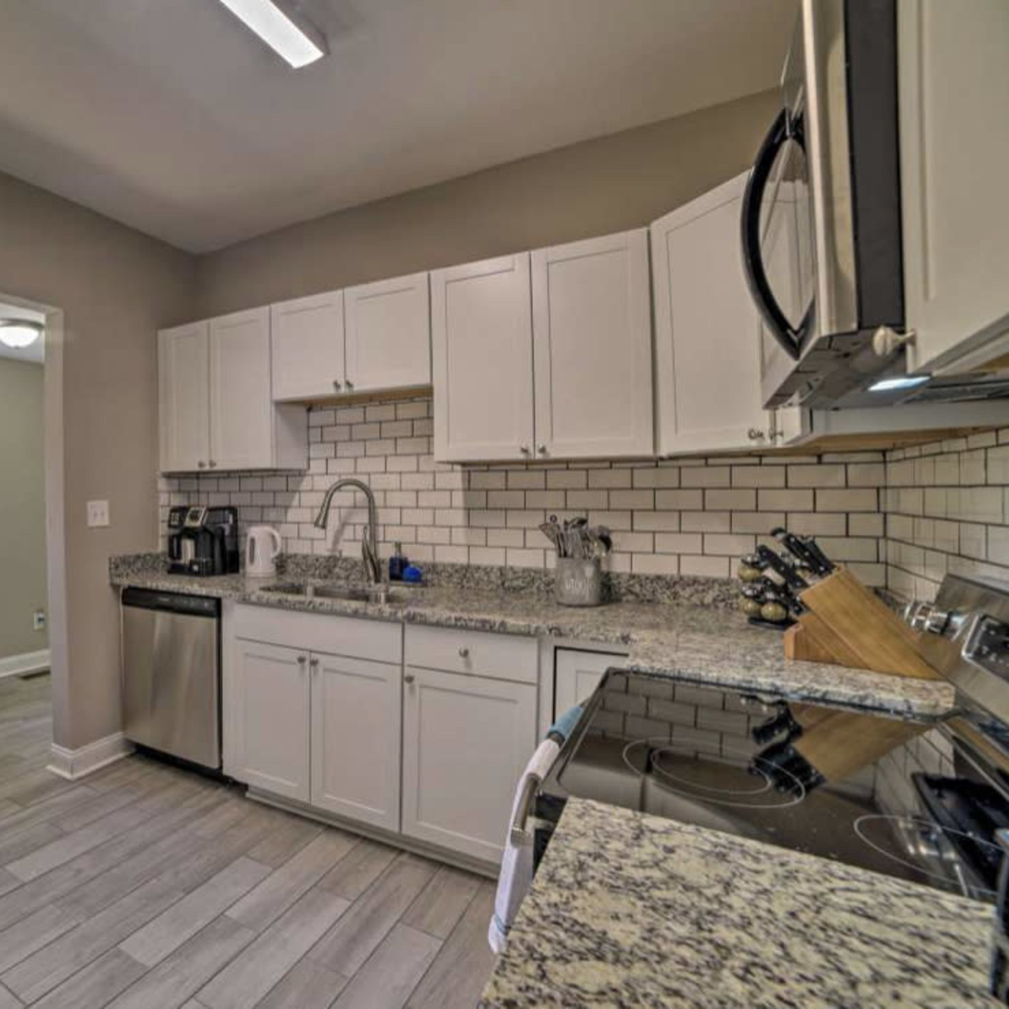 A modern kitchen features white cabinets, granite countertops, stainless steel appliances, and a view into an adjacent dining area with a table and chairs.