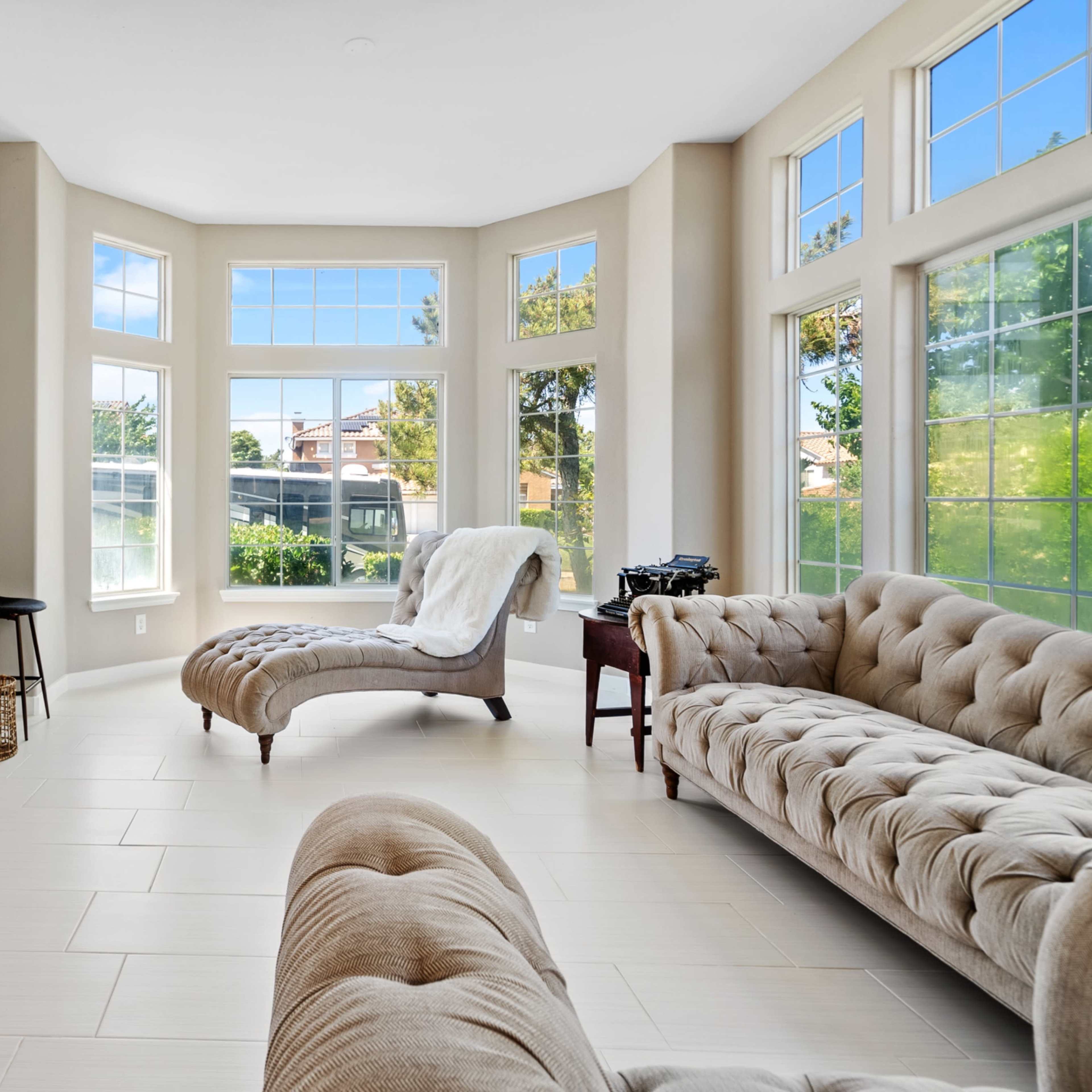 A bright living room features large windows, modern furniture, and a cozy seating area.