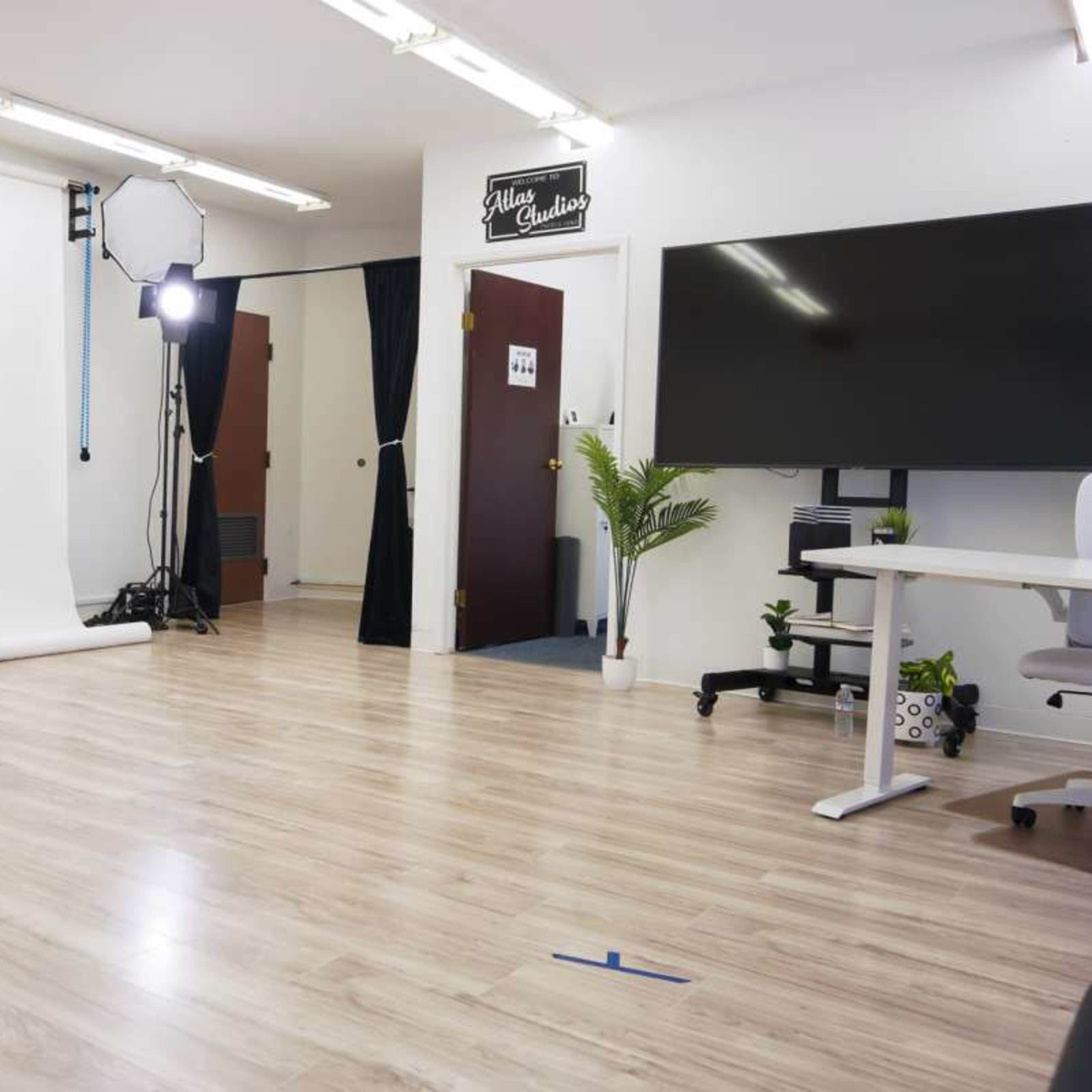 A well-lit photography studio featuring a white backdrop, studio lights, and a workspace with a desk and chair.