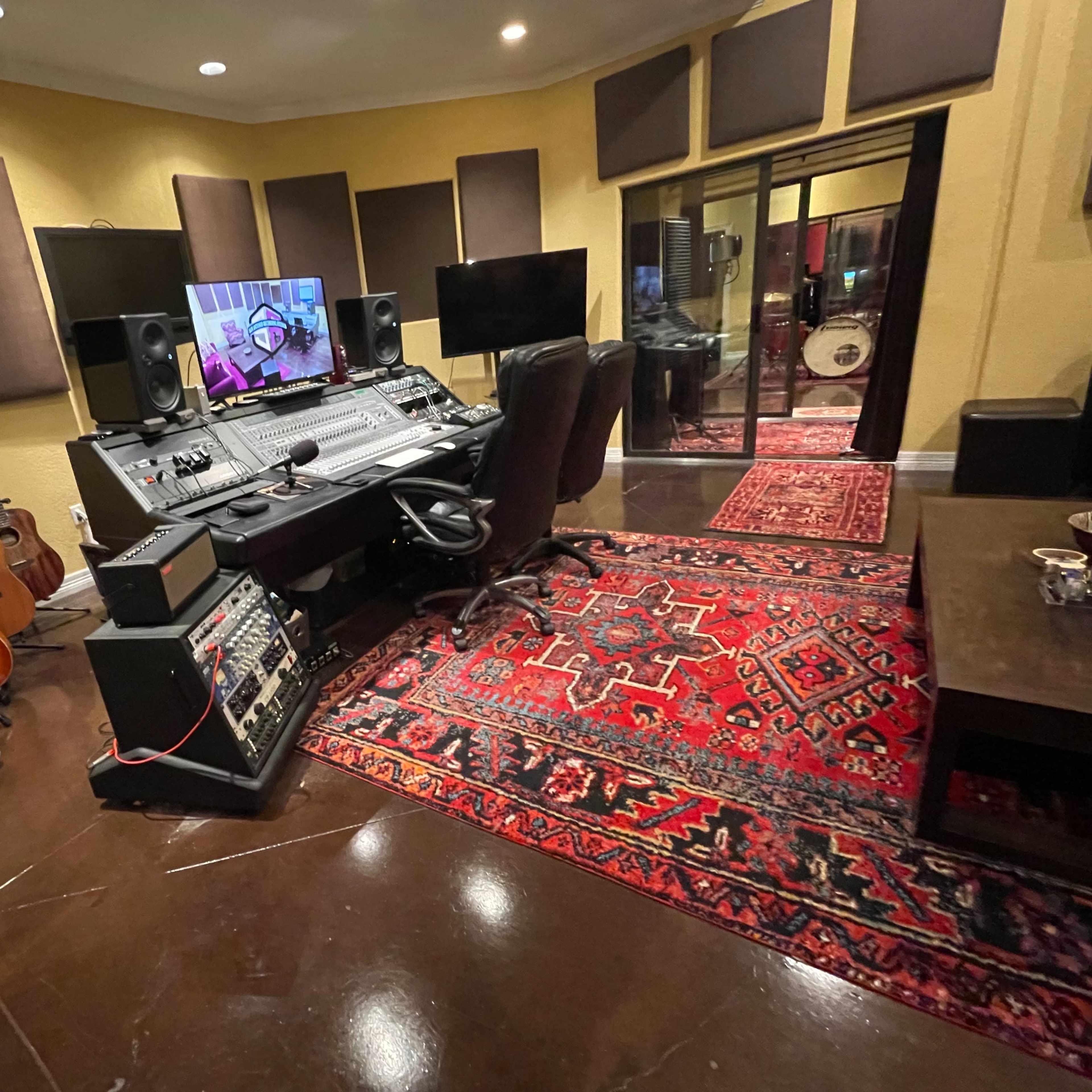 A music recording studio with a mixing console, multiple guitars, soundproofing panels, and a large area rug.