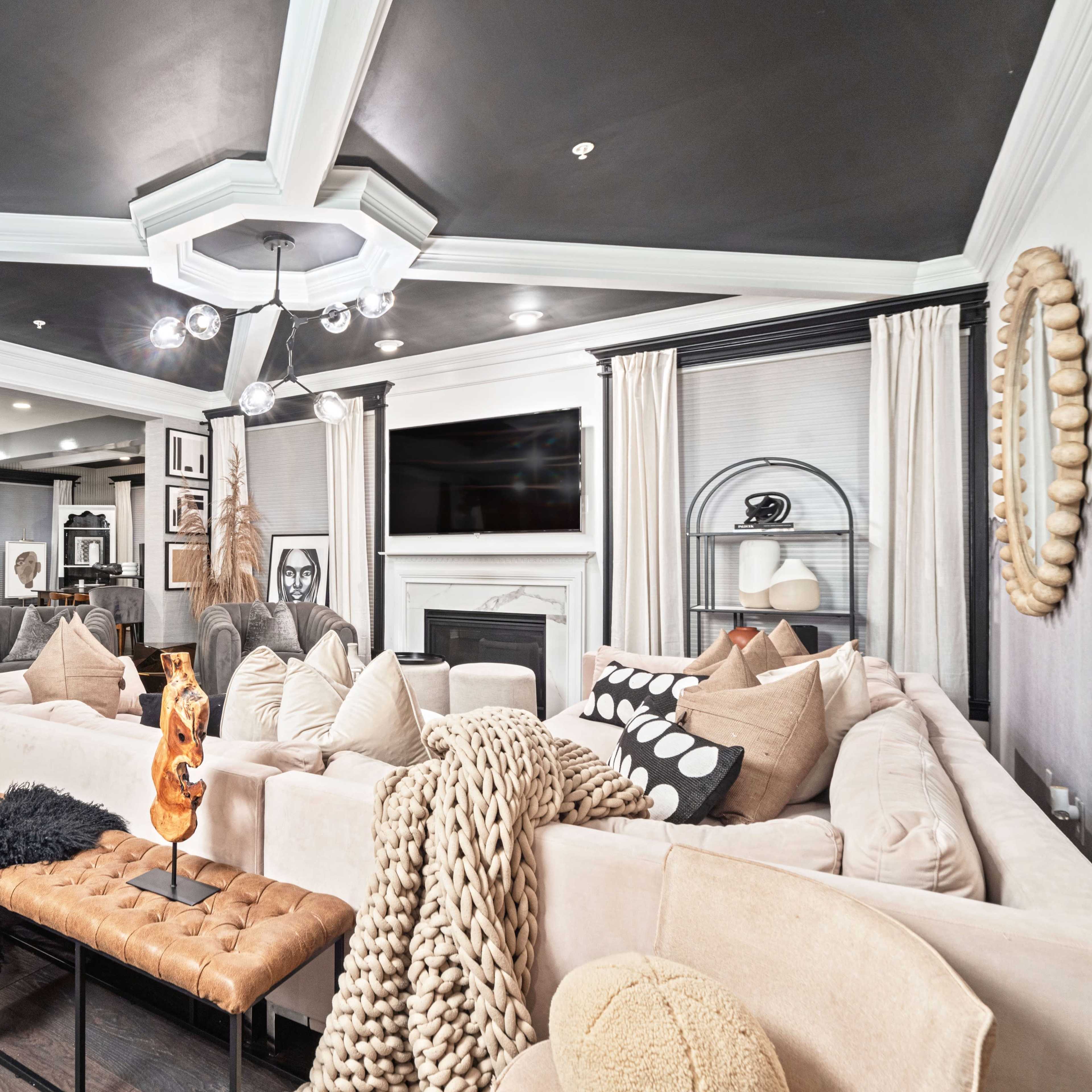 A modern living room features a large sectional sofa, a coffee table with decorative items, and a kitchen area visible in the background.