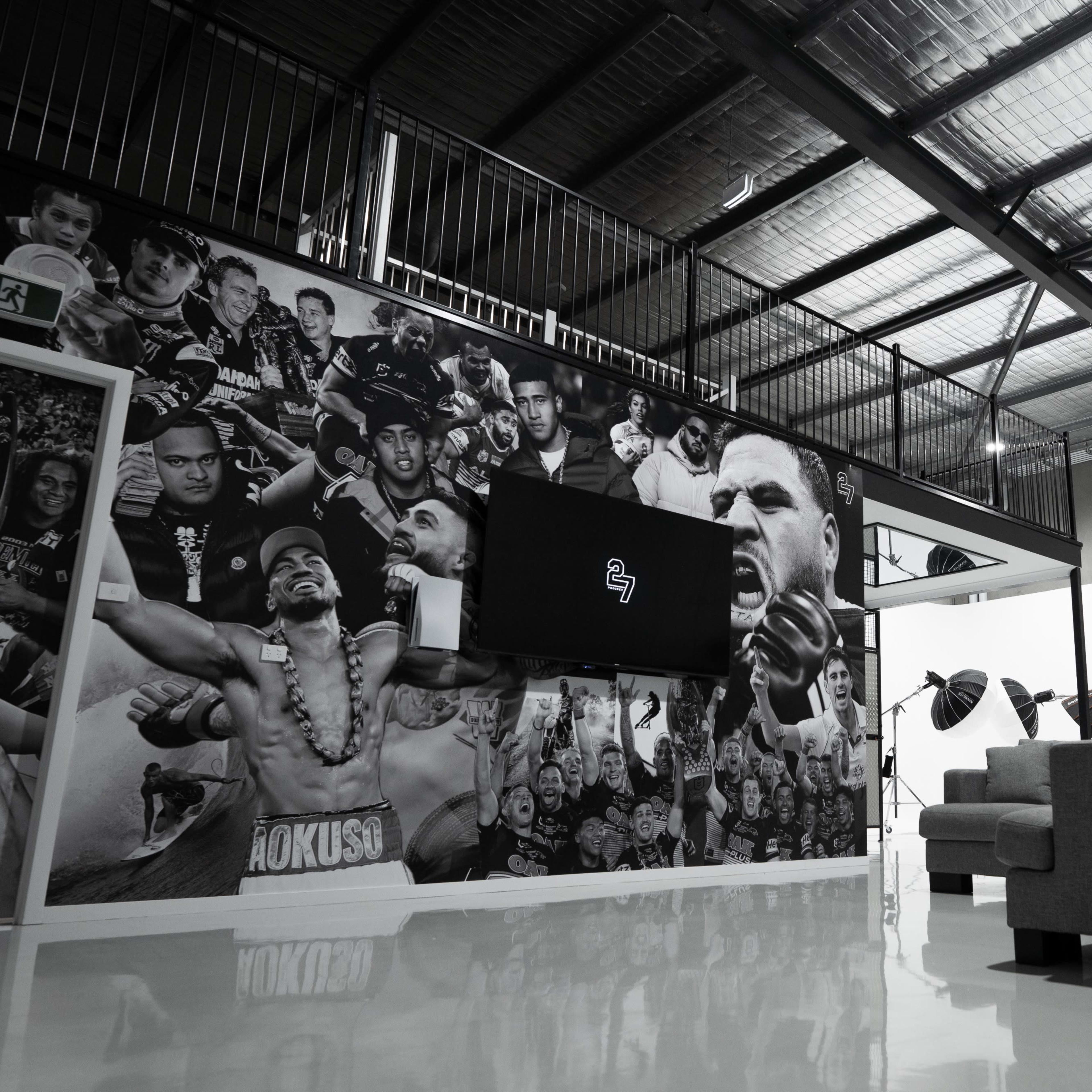 A modern indoor space featuring a large wall mural with various portraits, a mounted flat-screen TV, and a gray sofa.
