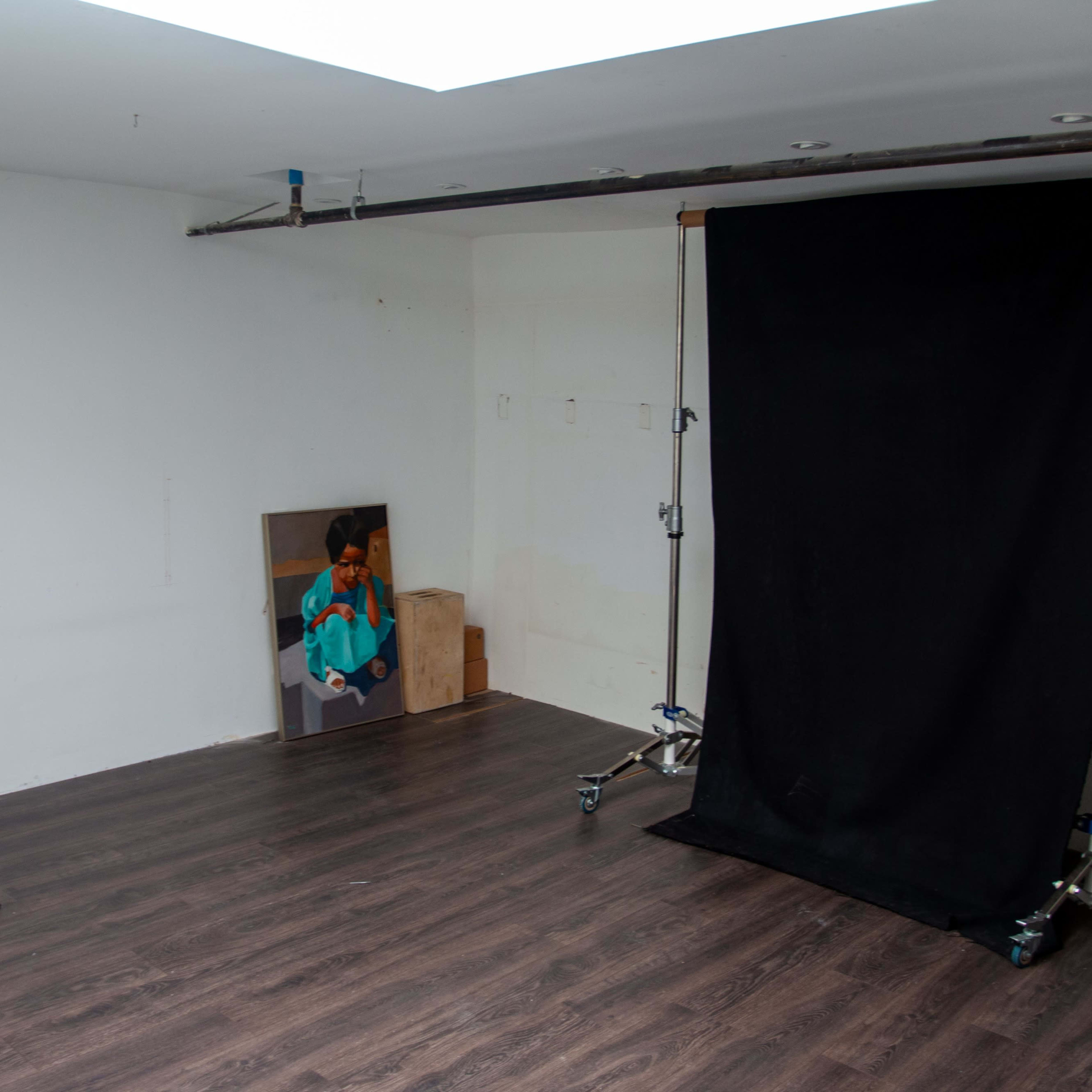 A photography studio with a black backdrop set up on a support stand, a wooden table, and a projector on the floor.
