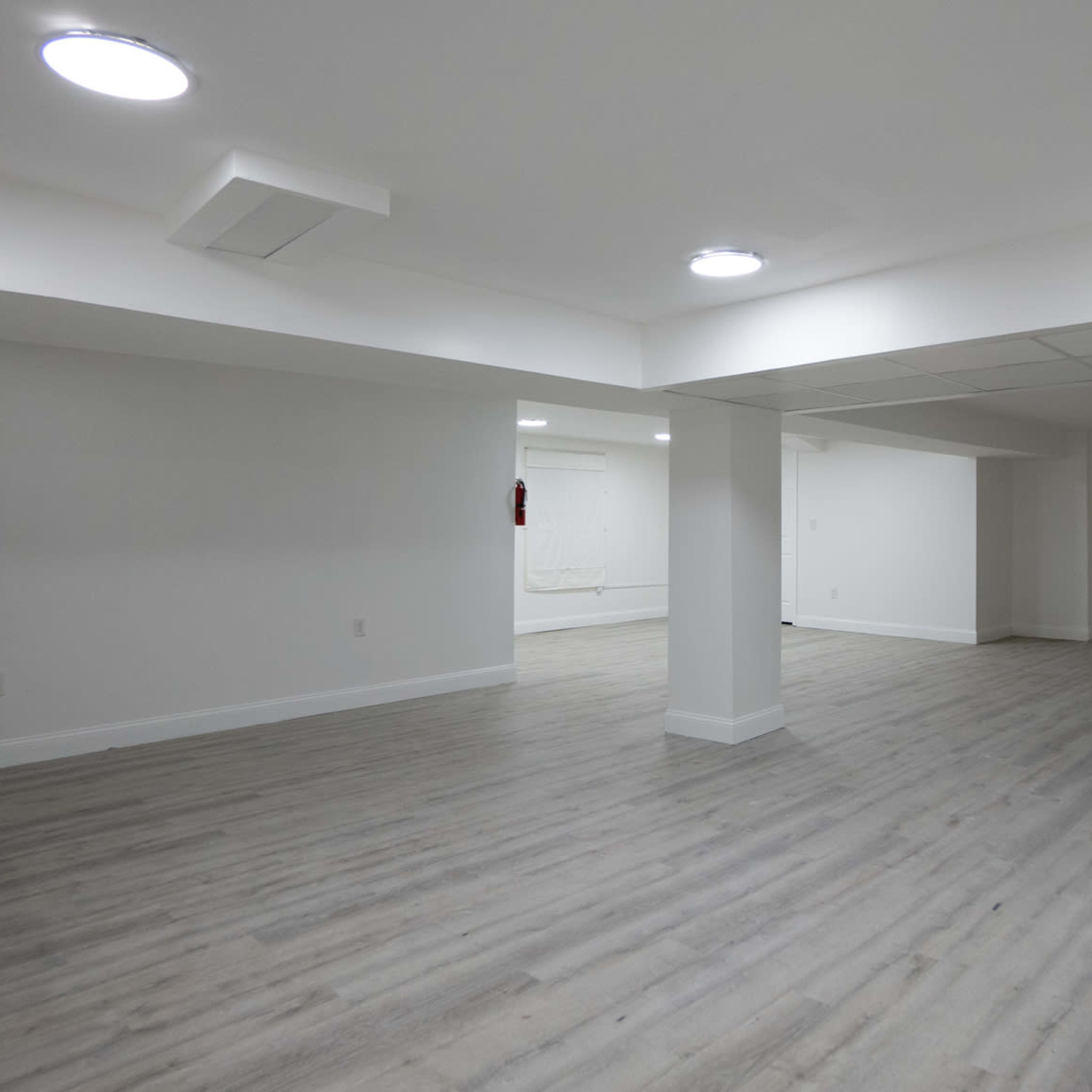 A large, empty room with light-colored wood flooring and recessed lighting on a white ceiling.