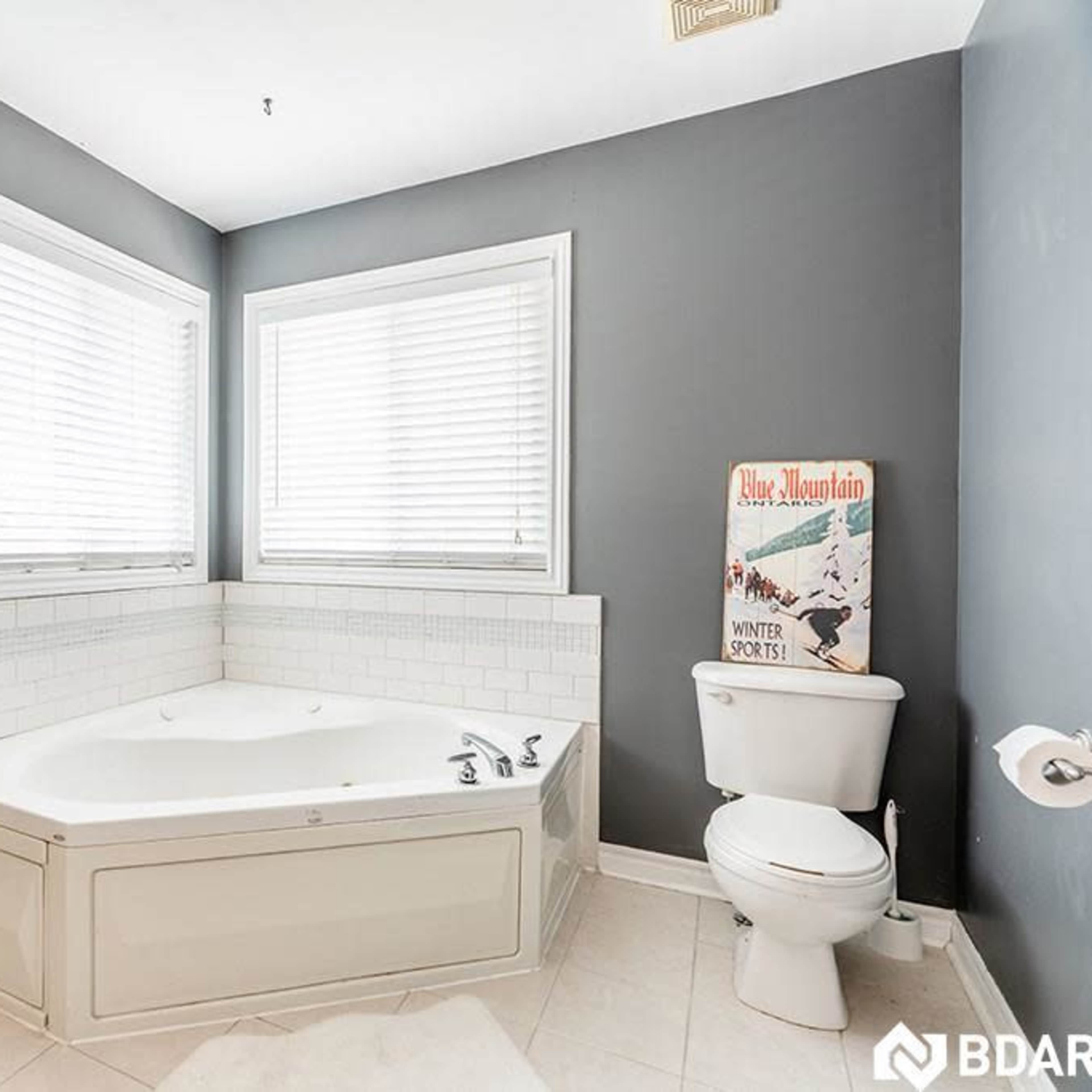 A bathroom featuring a corner jetted bathtub, a toilet, and large windows with blinds.