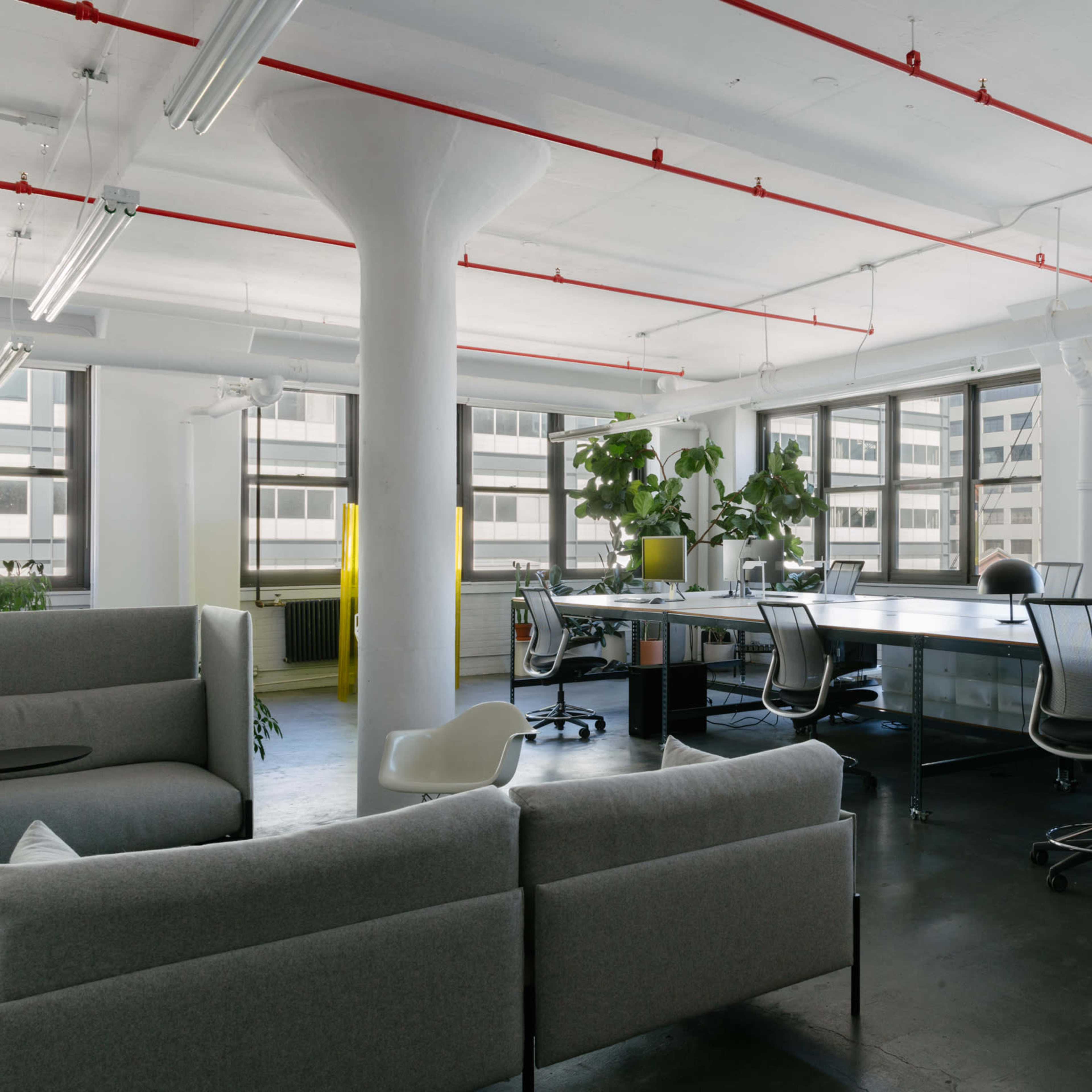 A modern office space with large windows, a long workspace table, and comfortable seating areas.