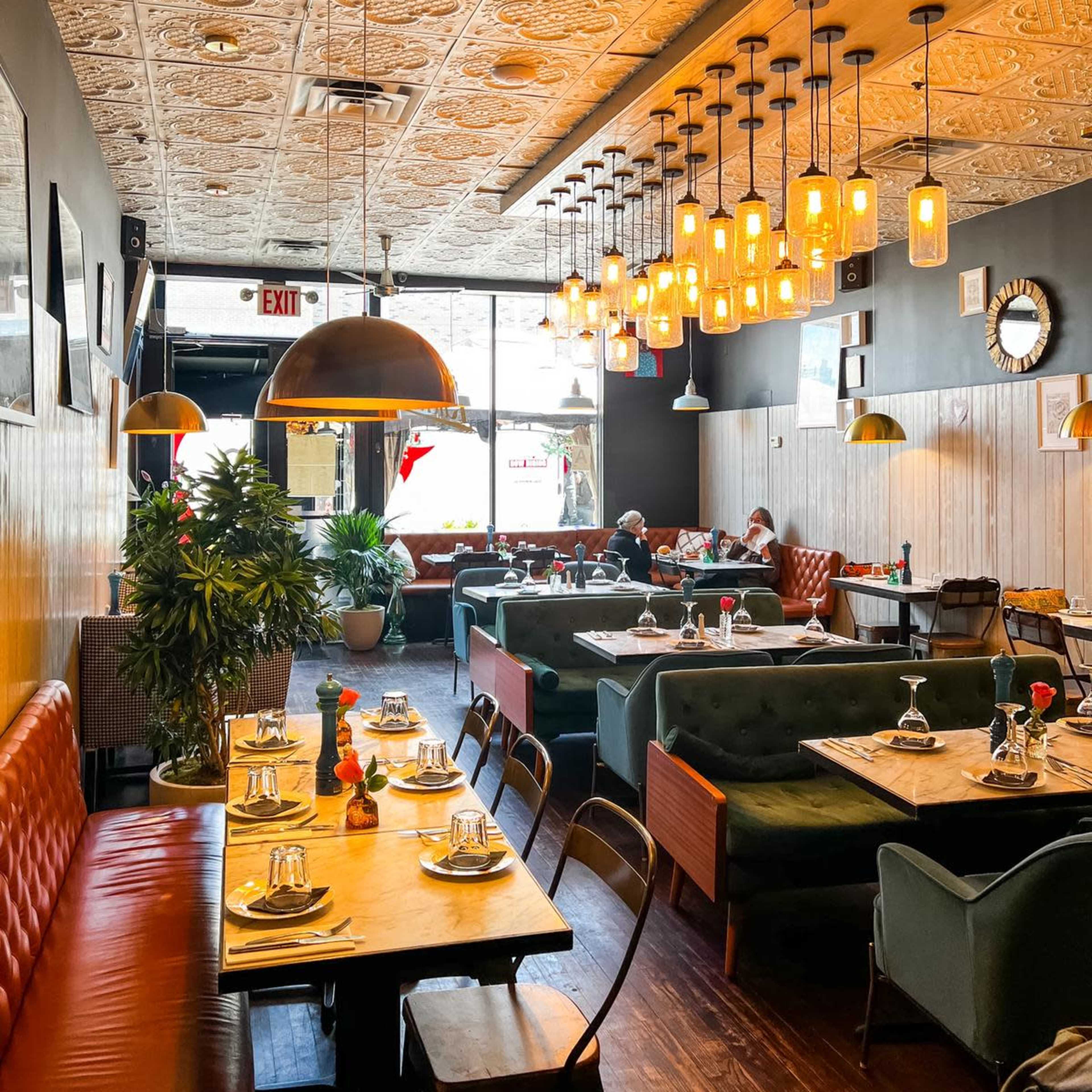 A modern restaurant interior with an ornate ceiling, wooden tables set for dining, and a mix of green and red seating arrangements.