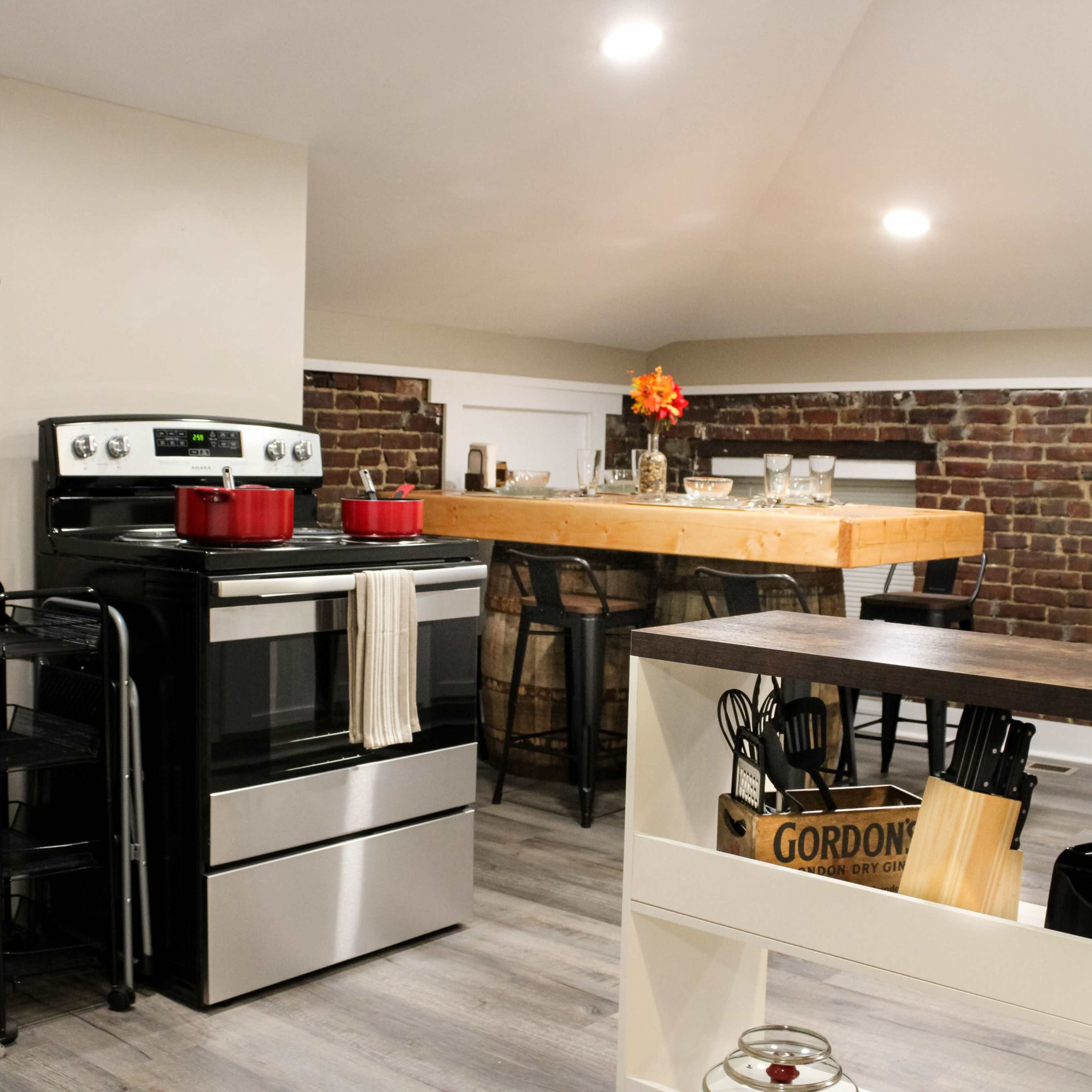 A modern kitchen features stainless steel appliances, a rustic wooden dining table, and exposed brick walls.