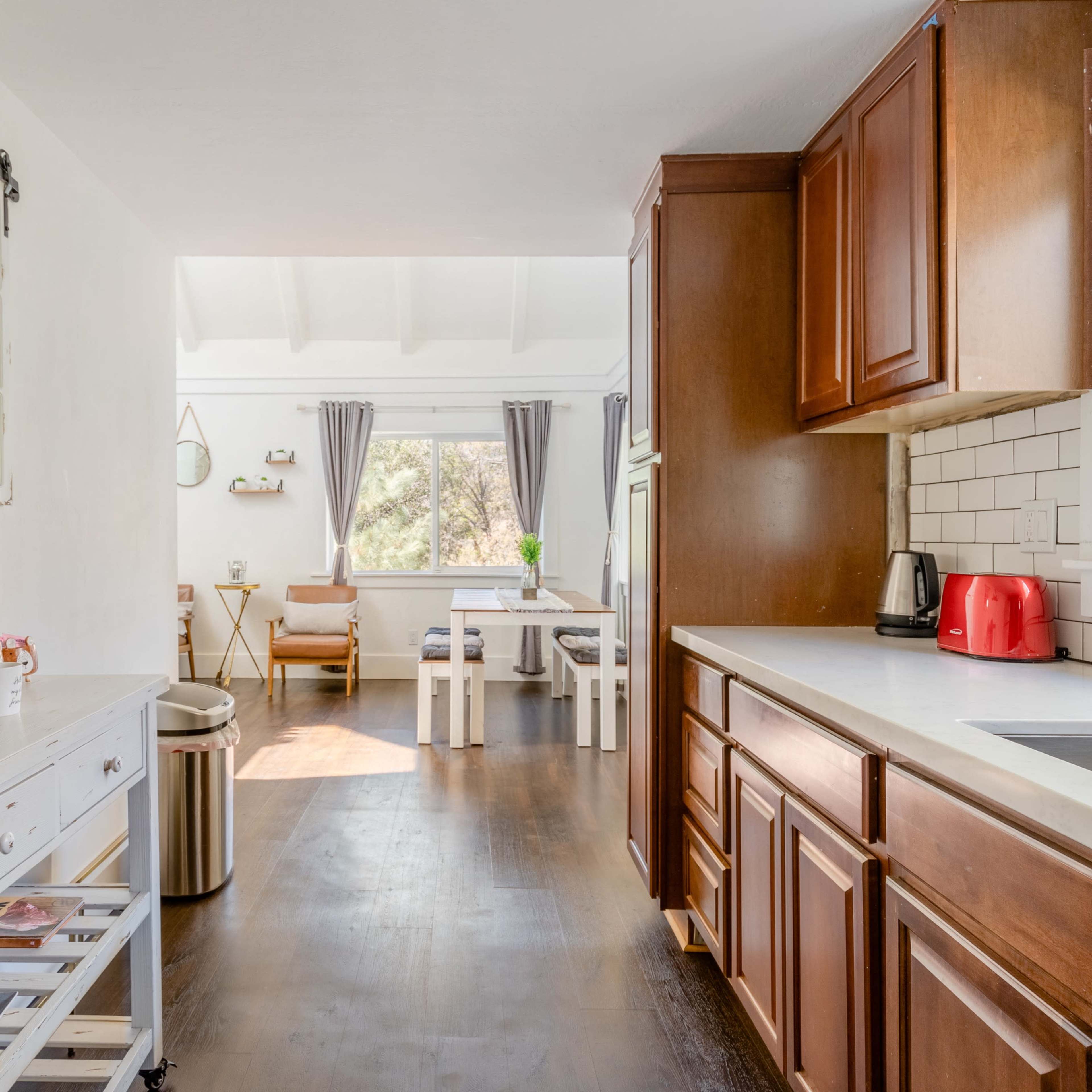 A bright kitchen with wooden cabinets and a coffee maker, leading into a dining area with a table and chairs.