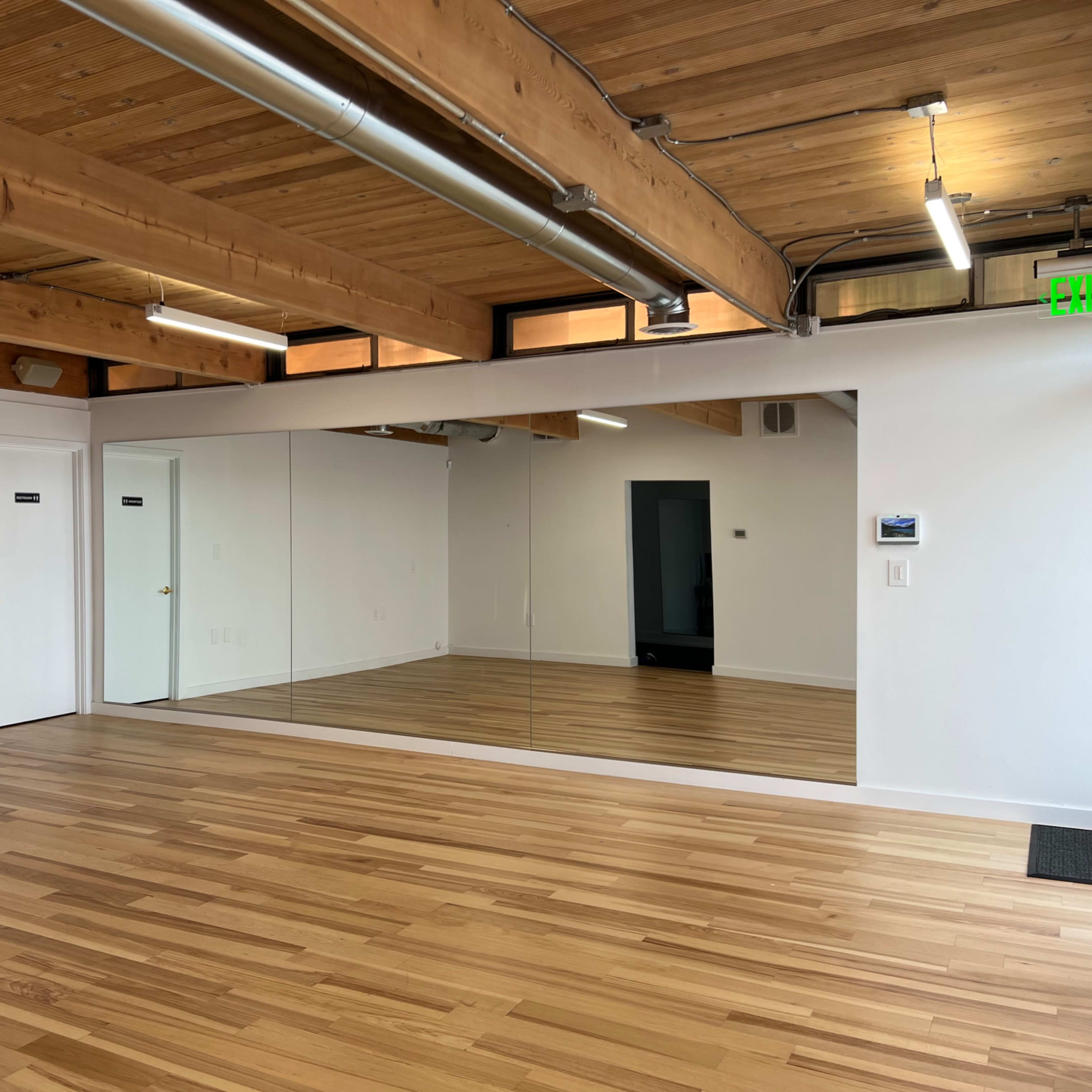 A spacious room with hardwood flooring, large mirrors on one wall, and exposed wooden beams on the ceiling.