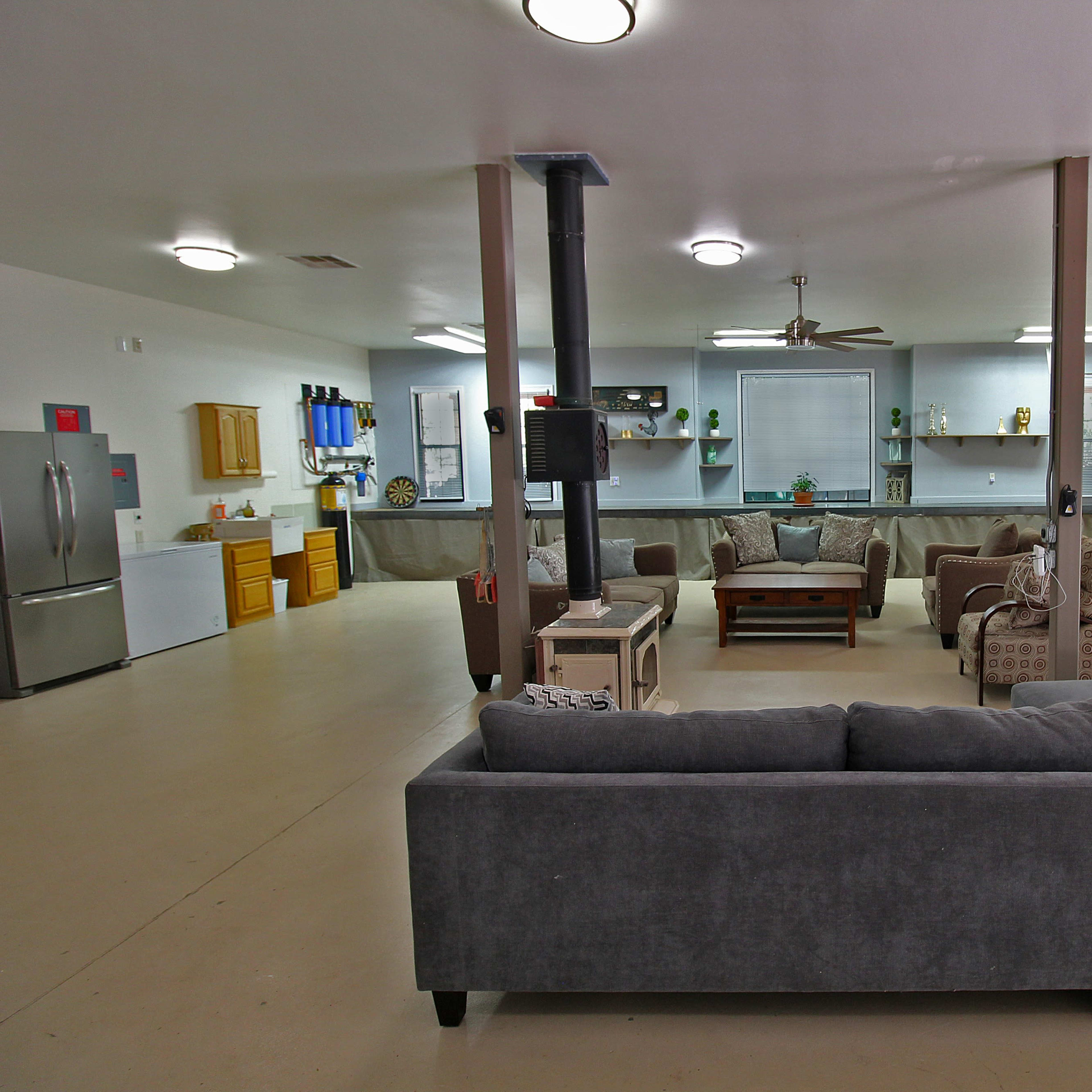 A spacious garage converted into a living area, featuring a sectional couch, coffee table, and a kitchen area with cabinets and appliances.