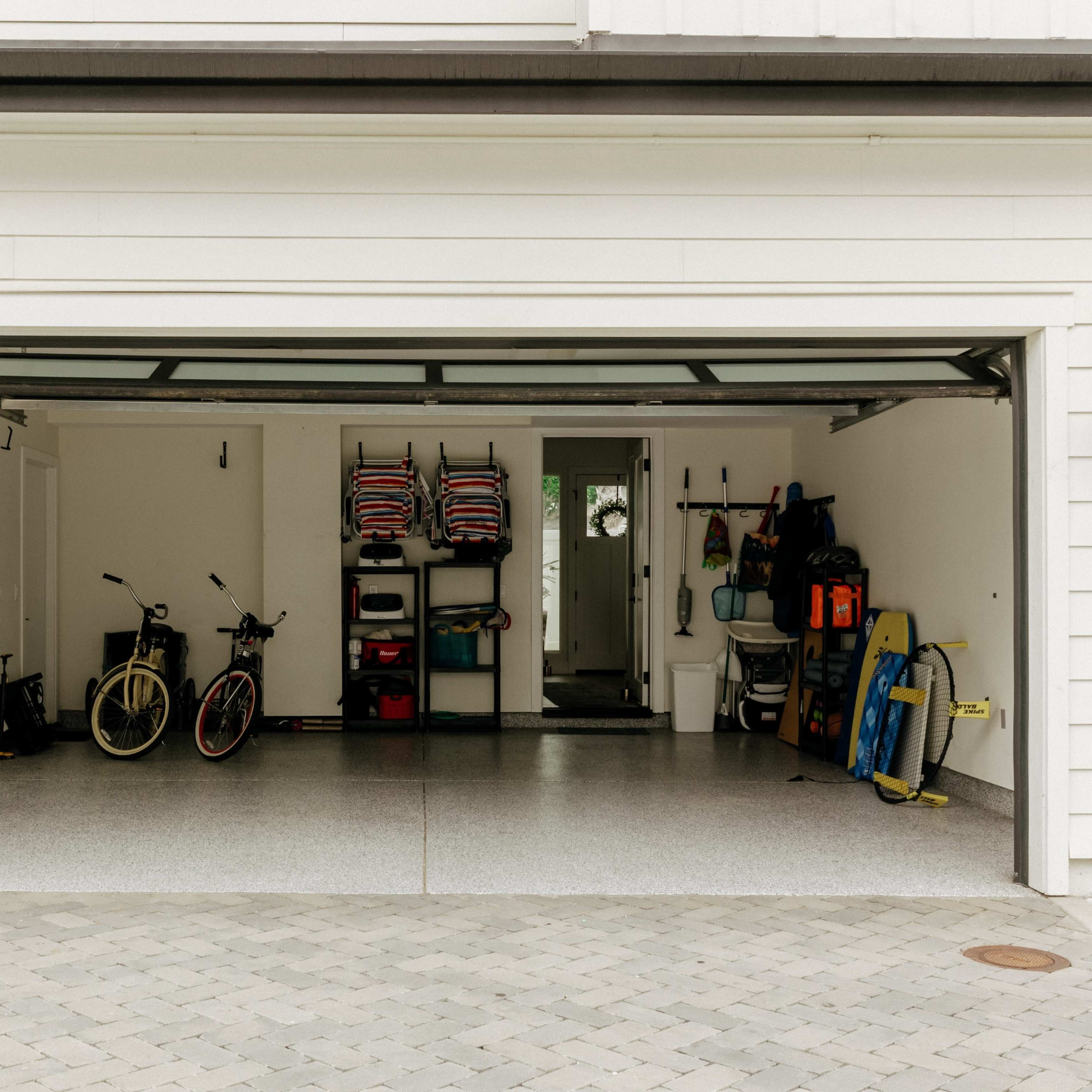 A garage with two bicycles, a shelving unit holding various items, and outdoor equipment is visible.