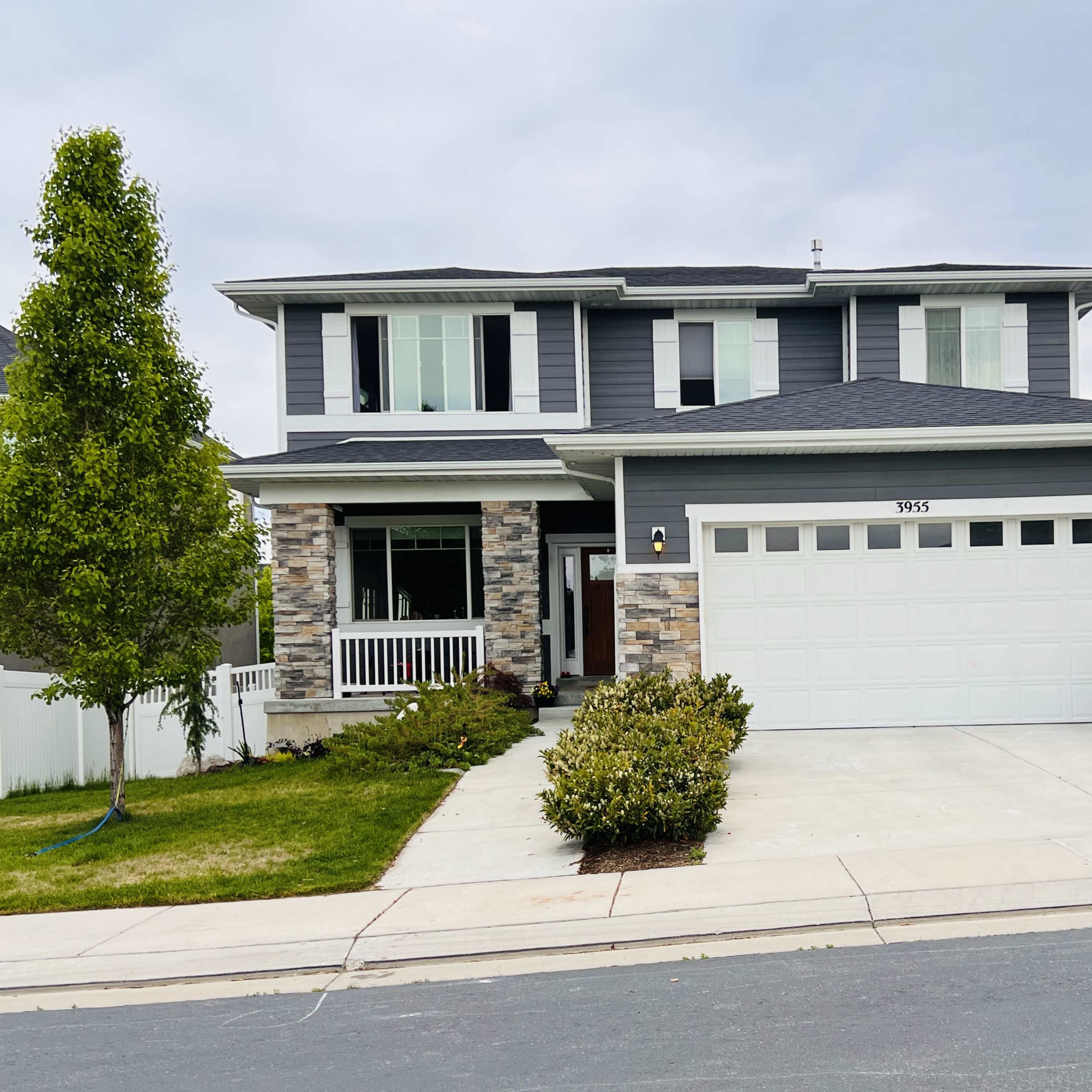A two-story gray house with stone accents, a two-car garage, and a well-manicured front yard.