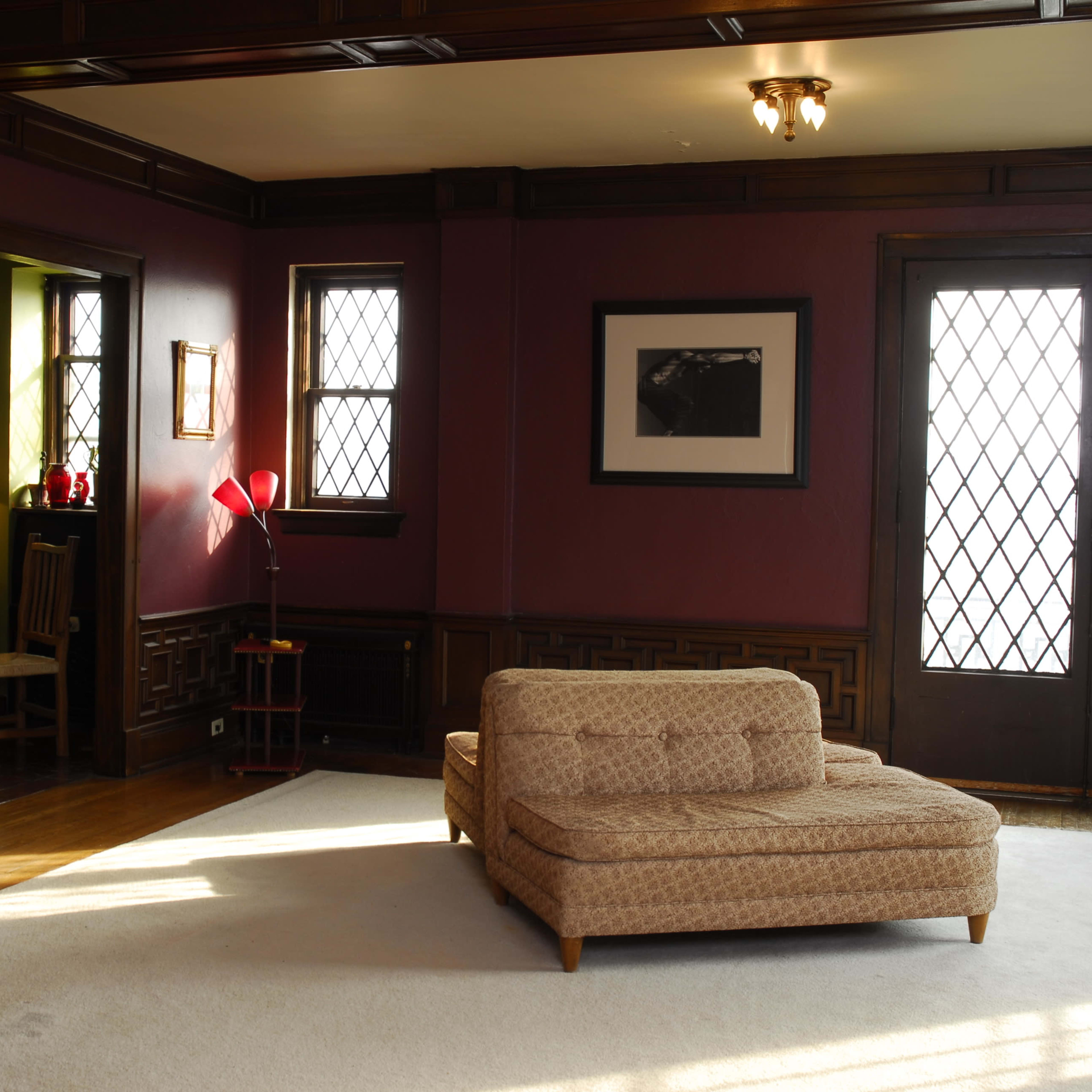 A spacious living room features a beige sectional sofa on a light rug, wooden accents, and large windows that provide natural light.