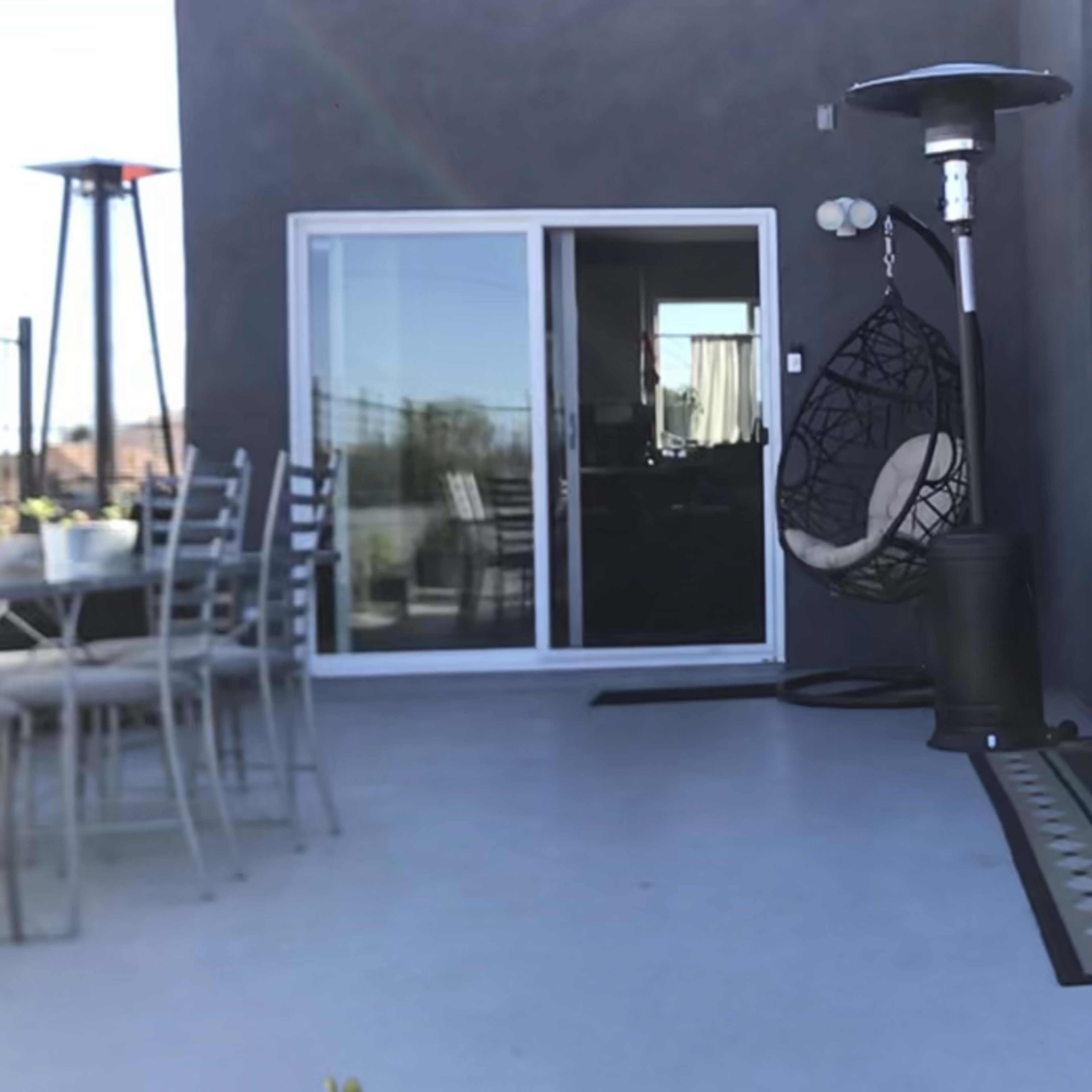 A patio area features a hanging chair, a dining table with chairs, and a fire pit, with a sliding glass door leading to an interior space.