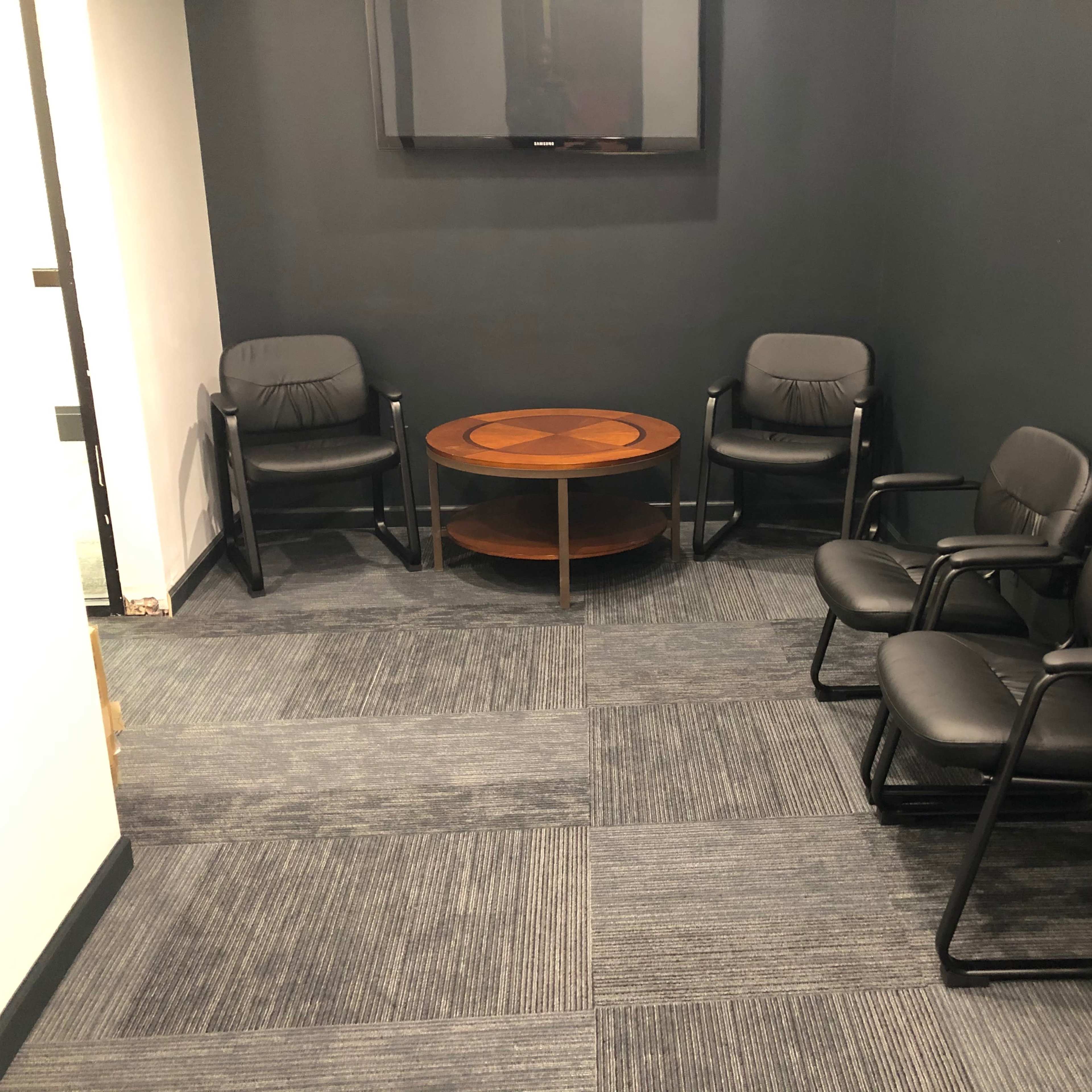 A small meeting room with four black chairs around a wooden coffee table and a wall-mounted television.