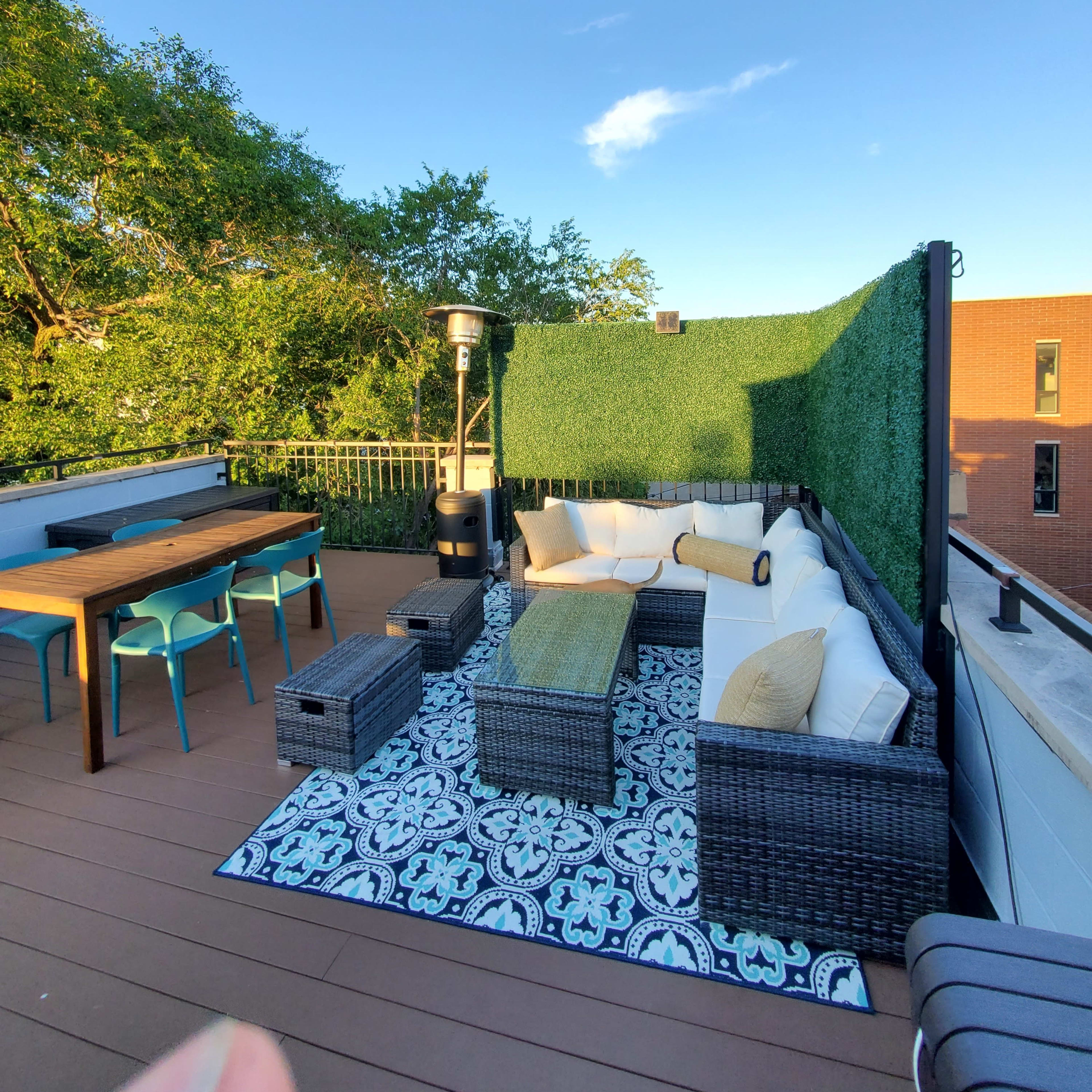 A rooftop terrace with a seating area, a dining table, and greenery along the perimeter.