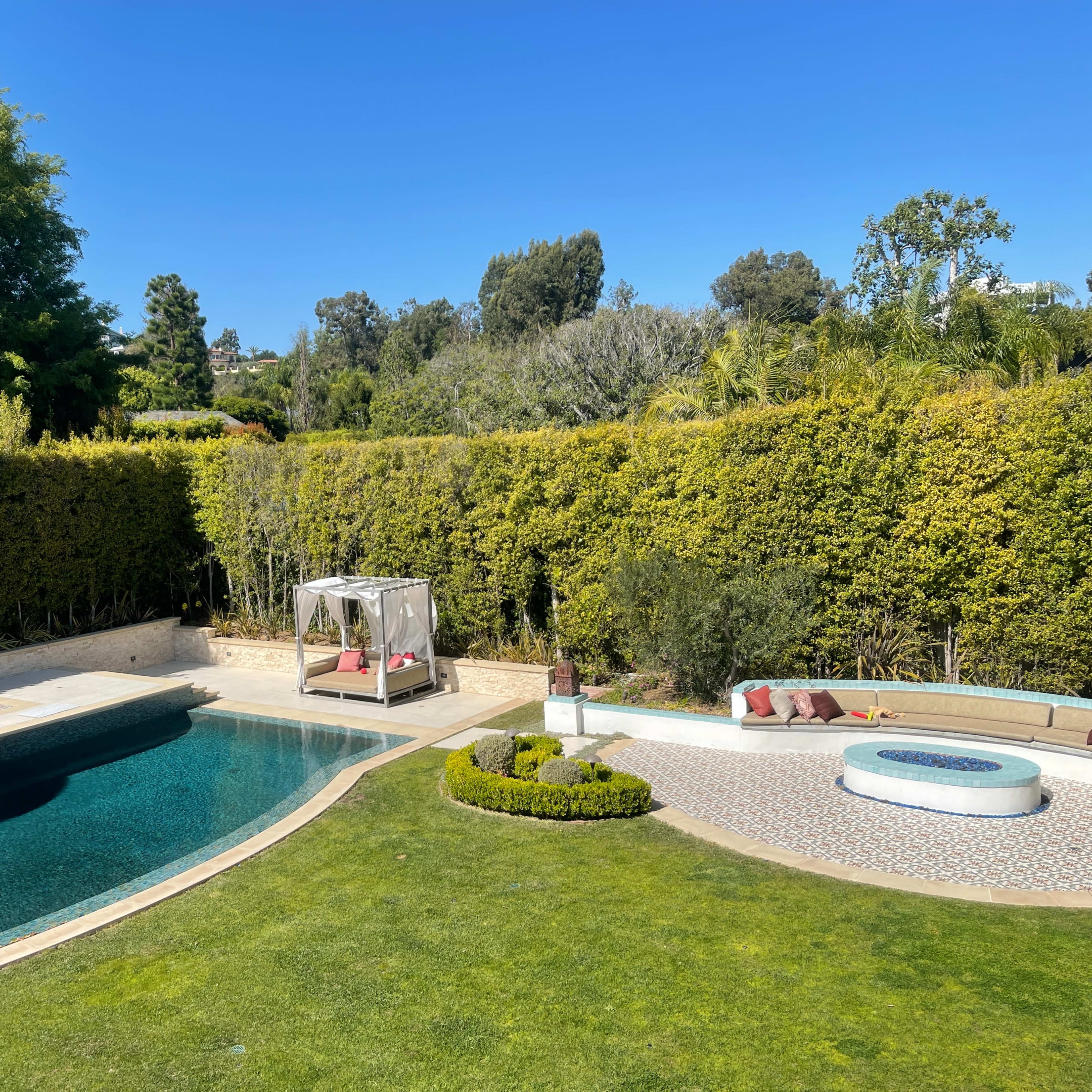A landscaped backyard with a swimming pool, a covered seating area, and neatly maintained greenery.