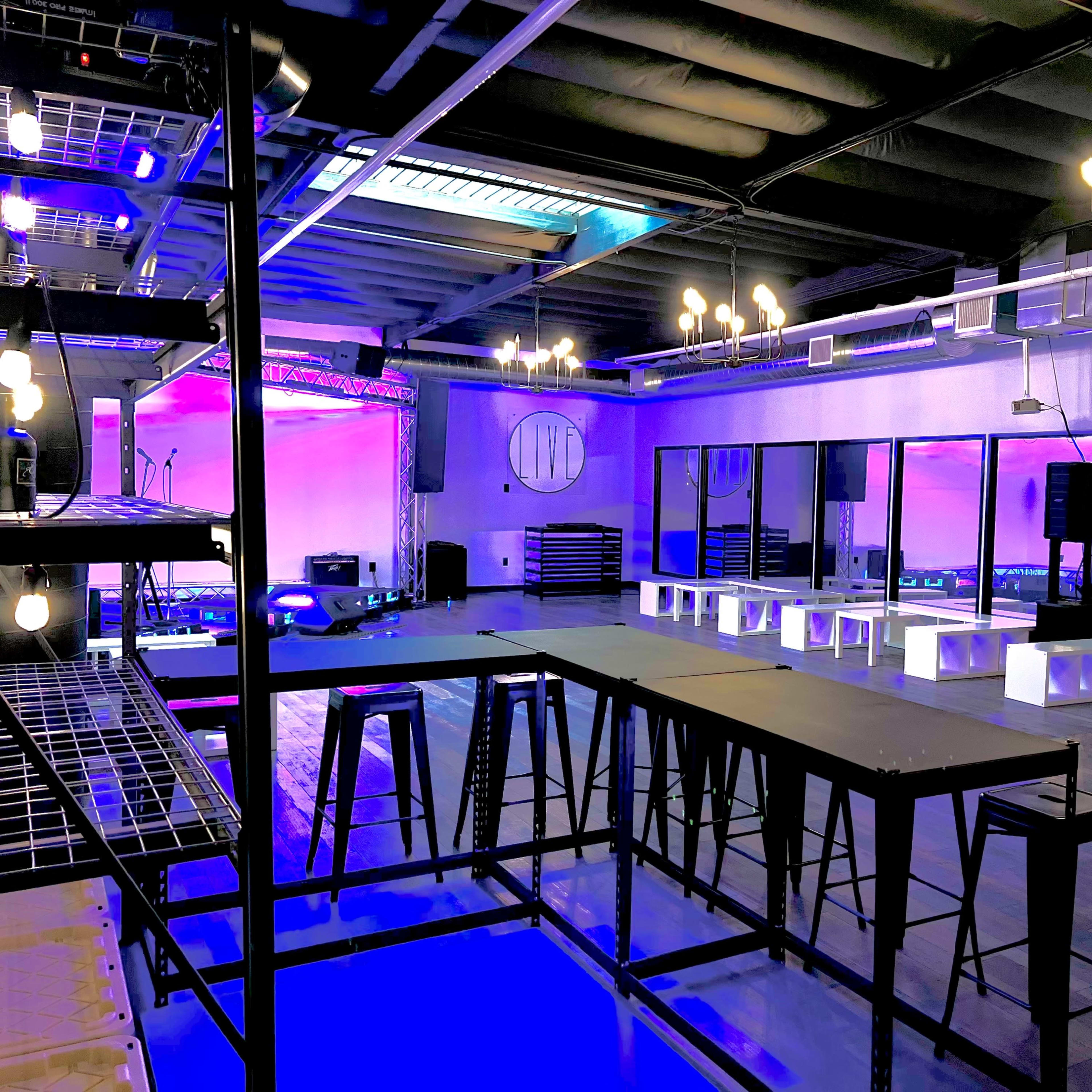 A modern event space with seating areas, a stage, and colorful lighting.
