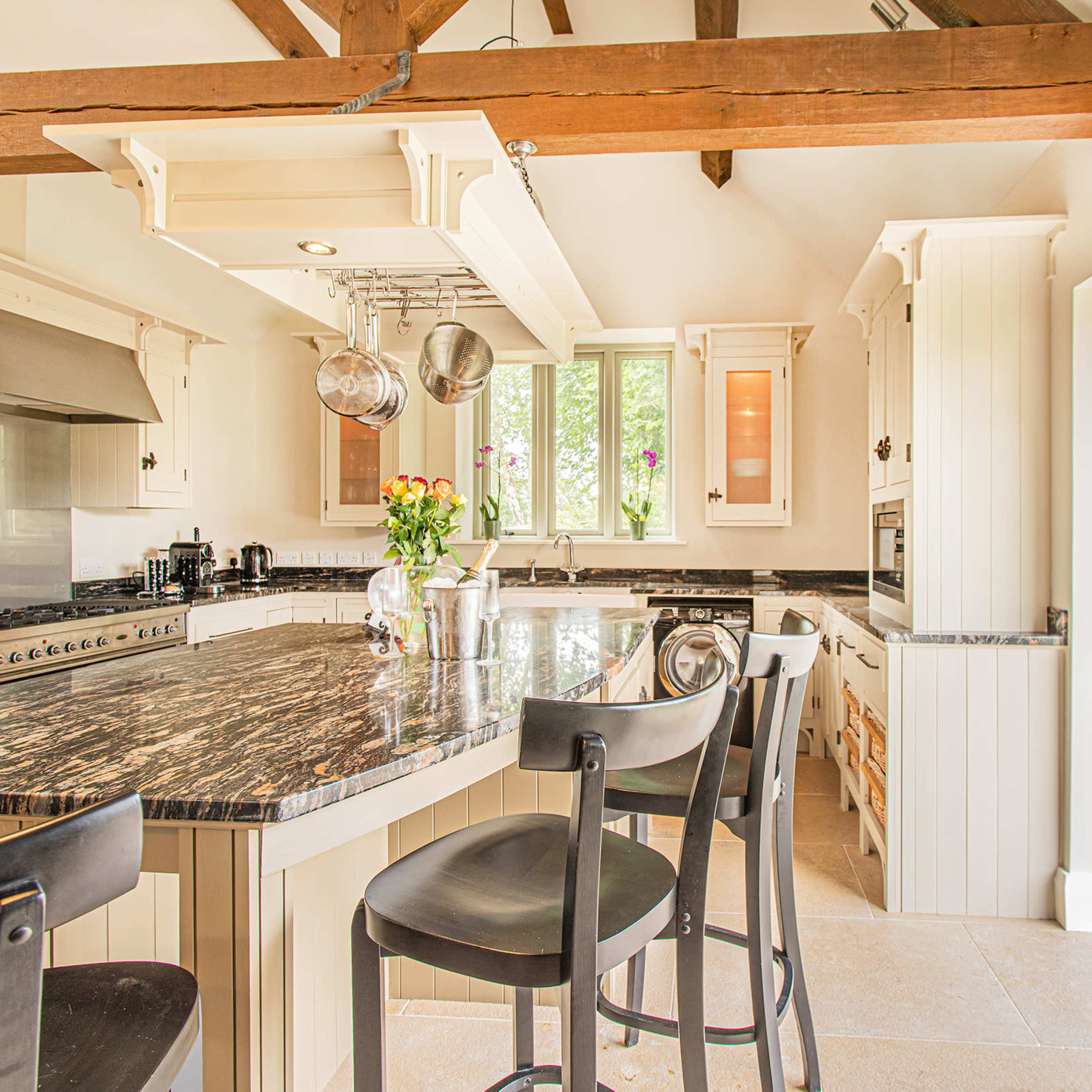 A modern kitchen features a large island with bar stools, stainless steel appliances, and opens to a stone patio through glass doors.