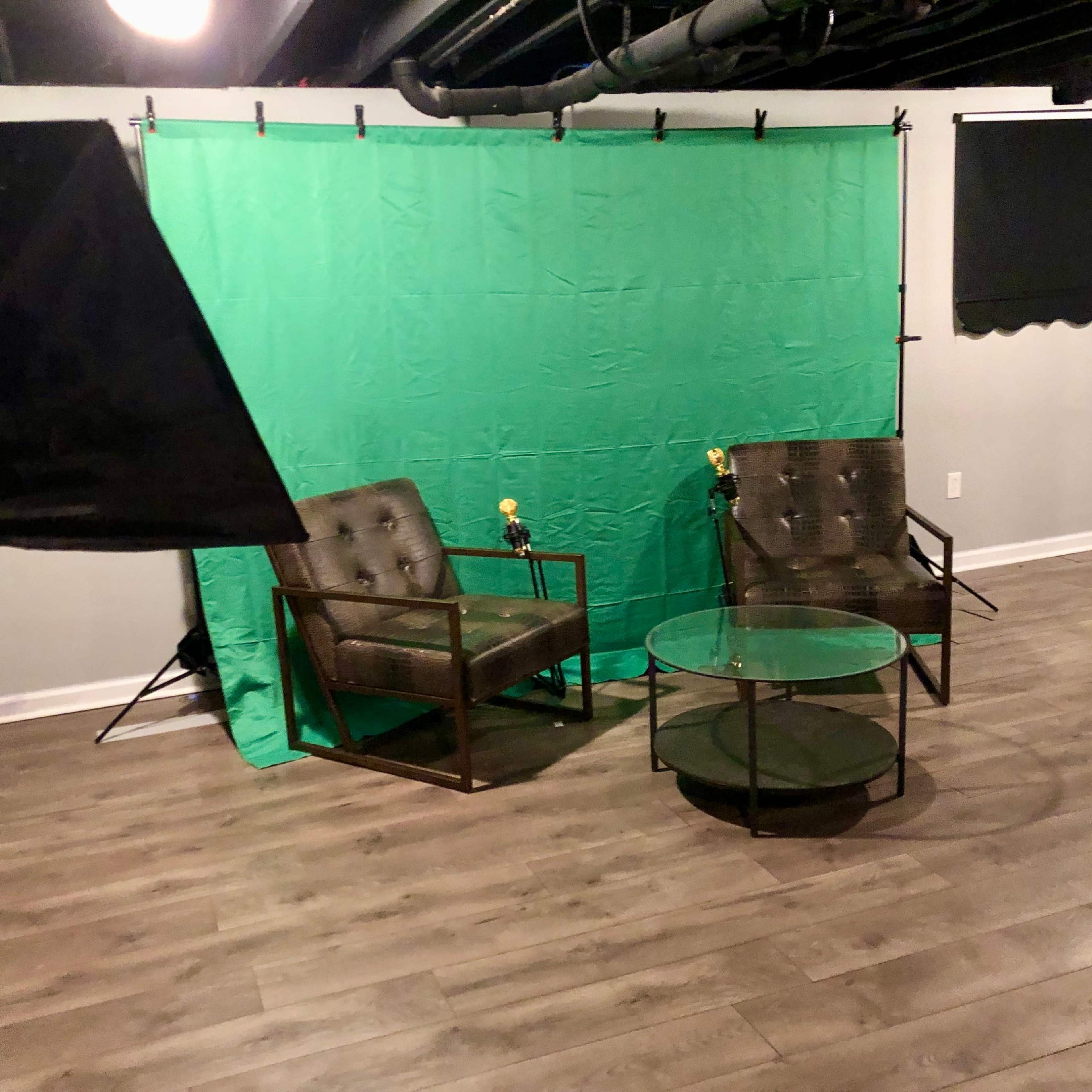 A studio setup with two chairs, a glass table, and a green backdrop, illuminated by softbox lighting.