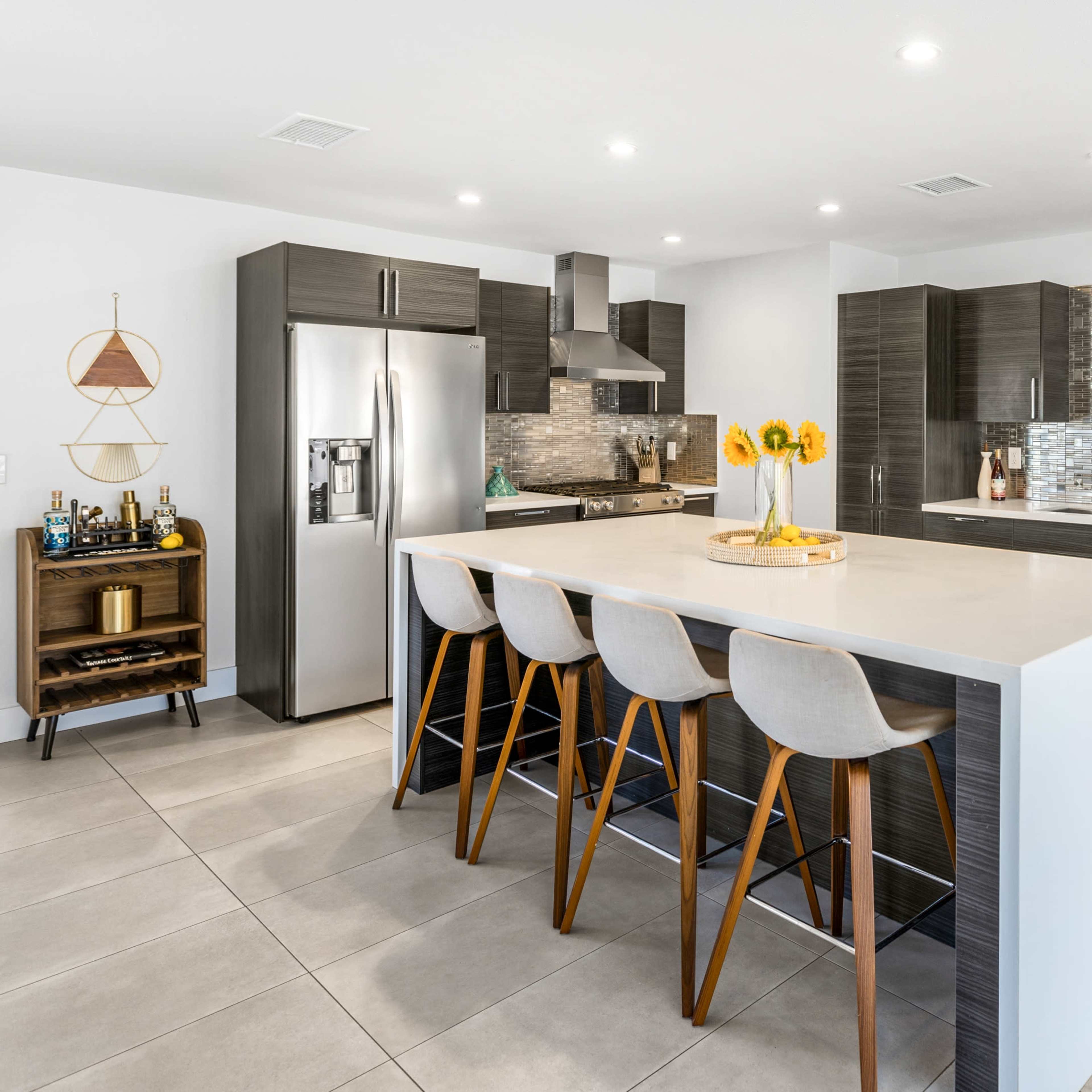 A modern kitchen with dark cabinetry, stainless steel appliances, and a large island with bar stools.