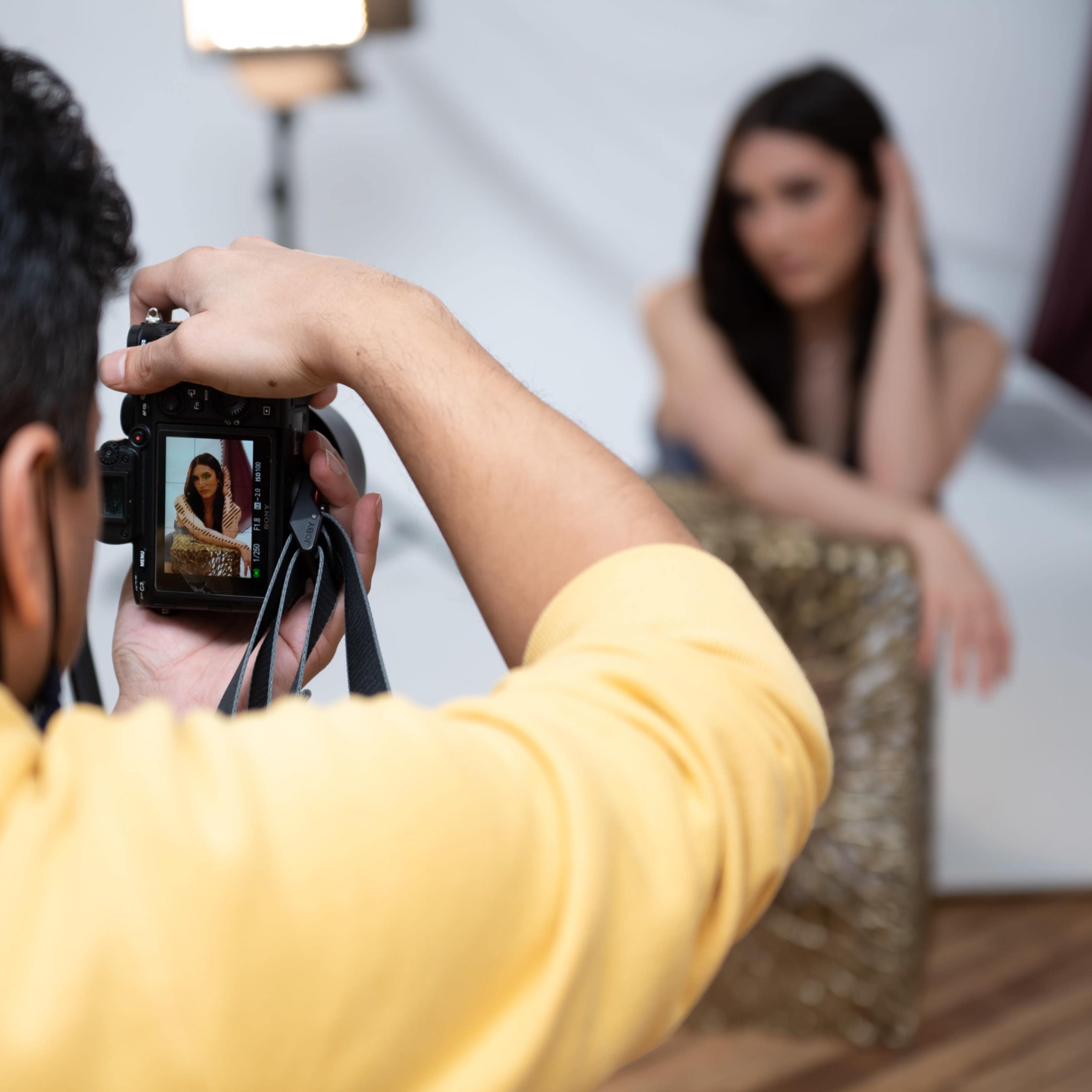 A photographer takes a portrait of a model who is posing with a decorative backdrop.