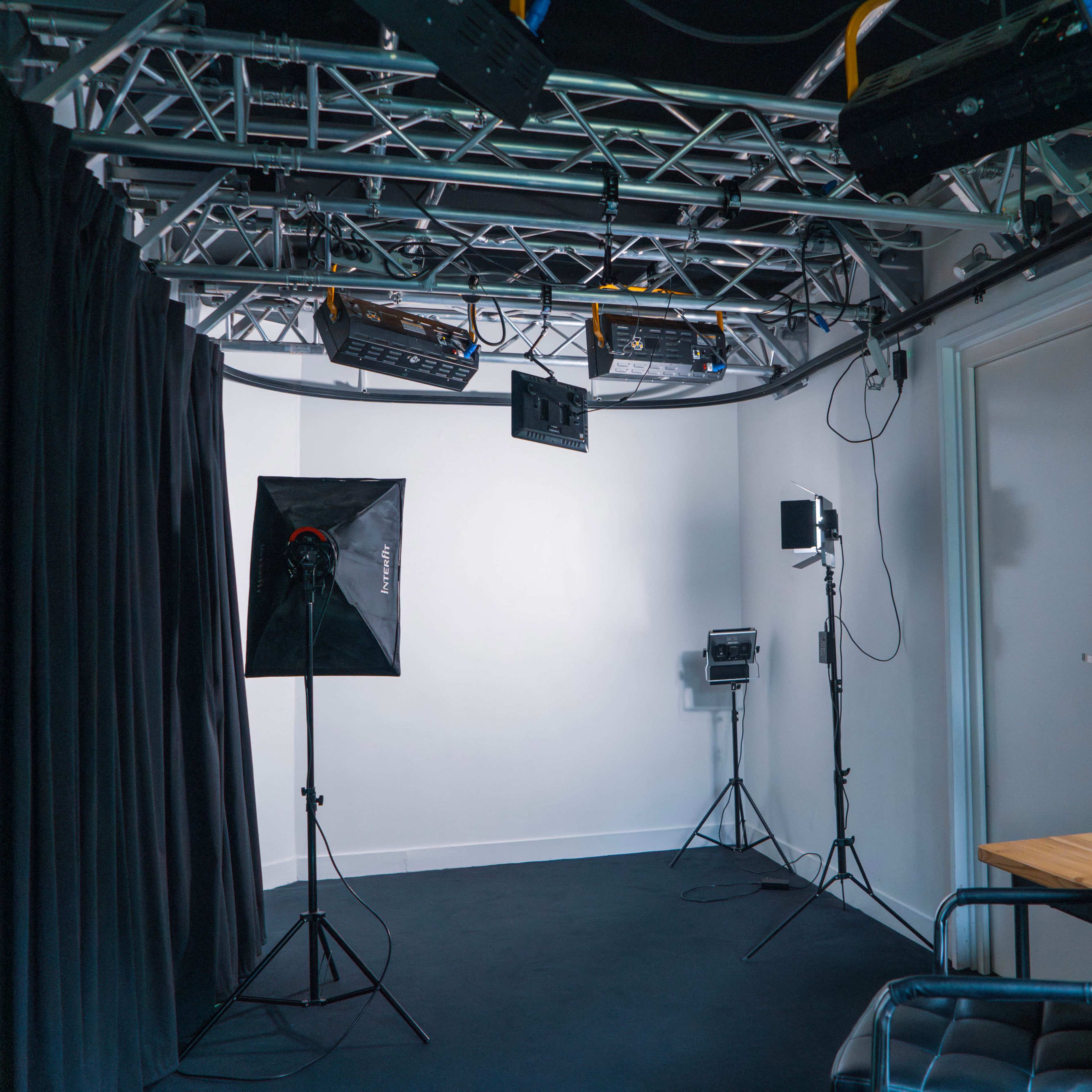 A studio setup featuring a dark backdrop, lighting equipment, and a desk with a computer chair and an Apple computer.