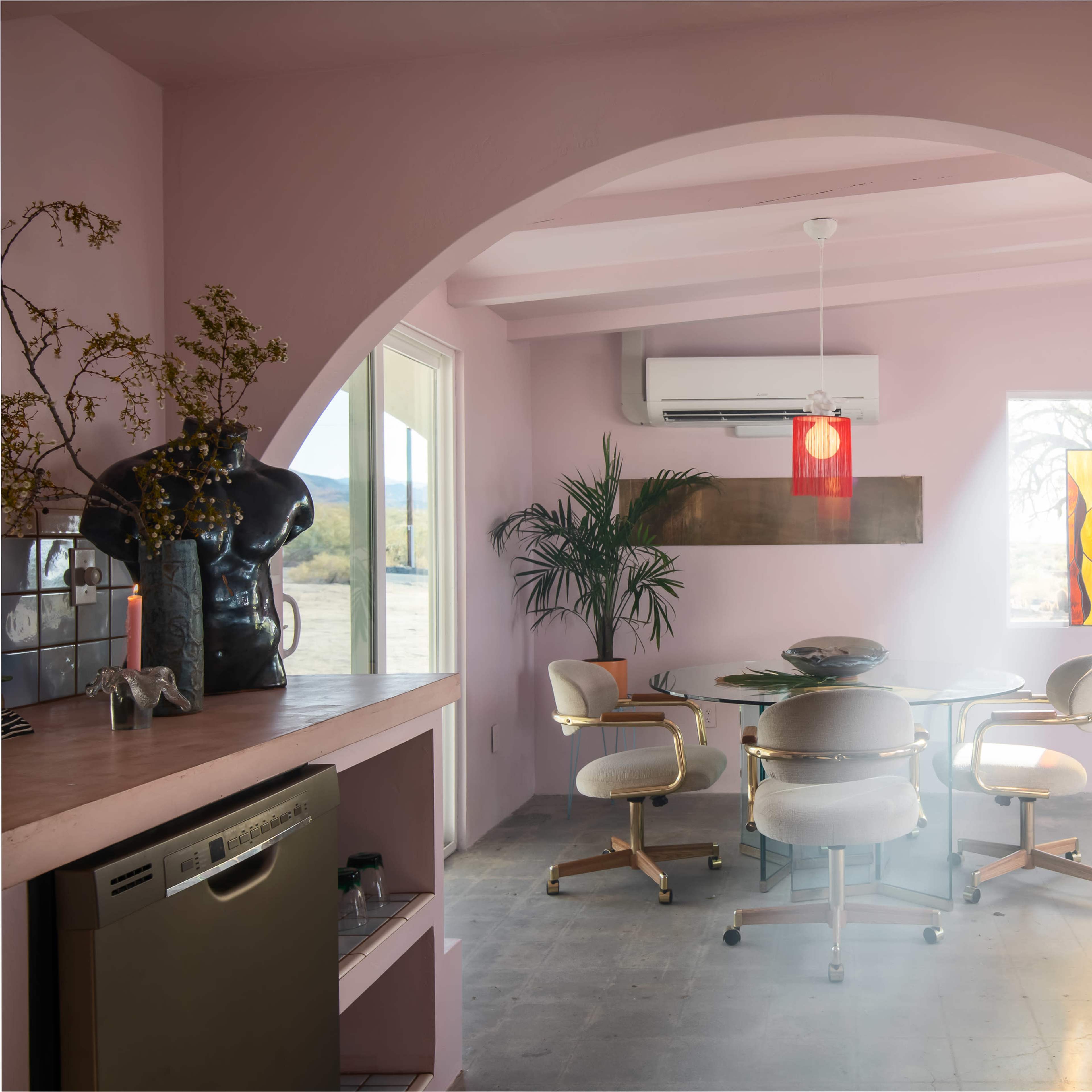 A modern dining area features a round table with six chairs, surrounded by pastel walls and illuminated by artful light streaming through a stained glass window.