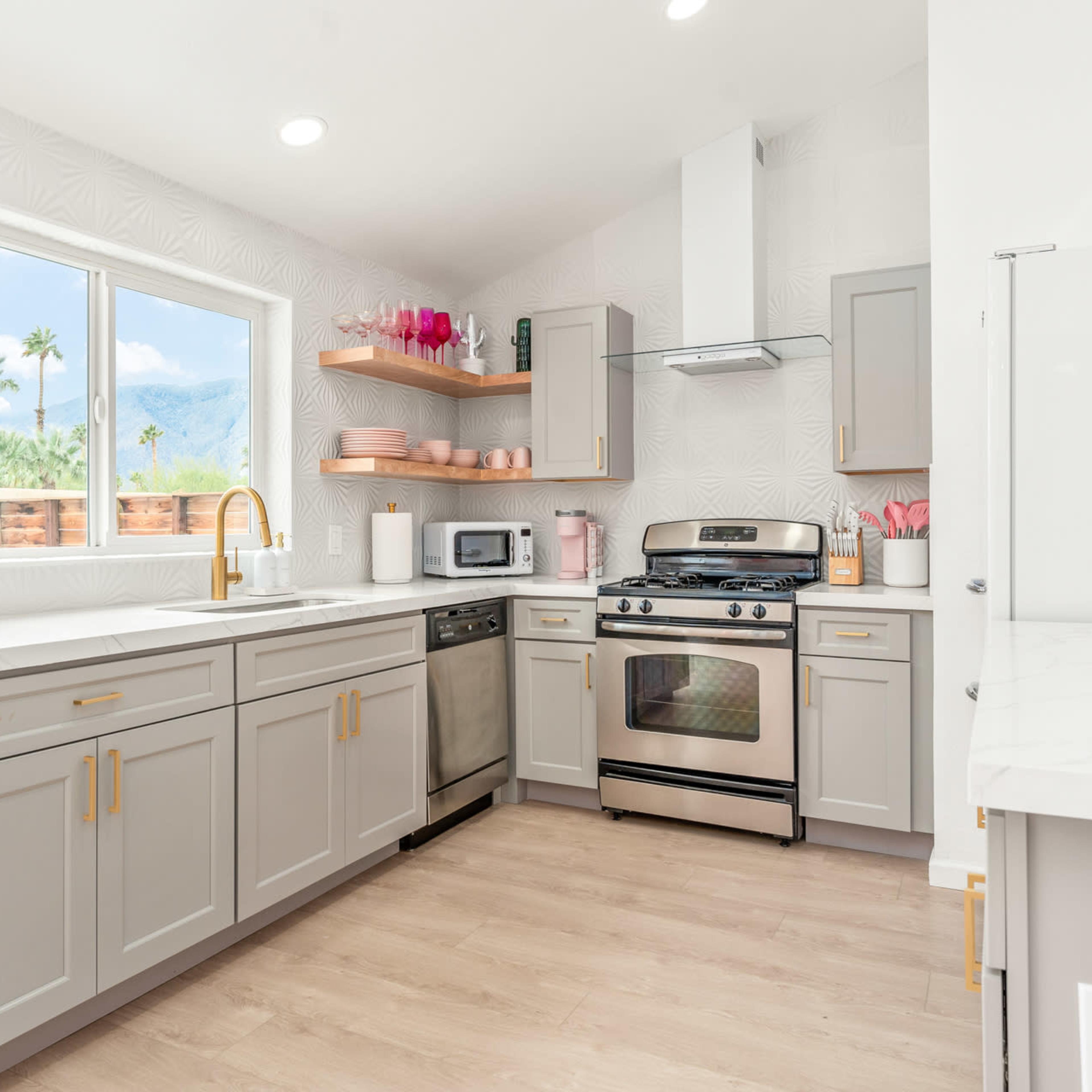 A modern kitchen featuring light gray cabinets, stainless steel appliances, and a window with a view of palm trees outside.