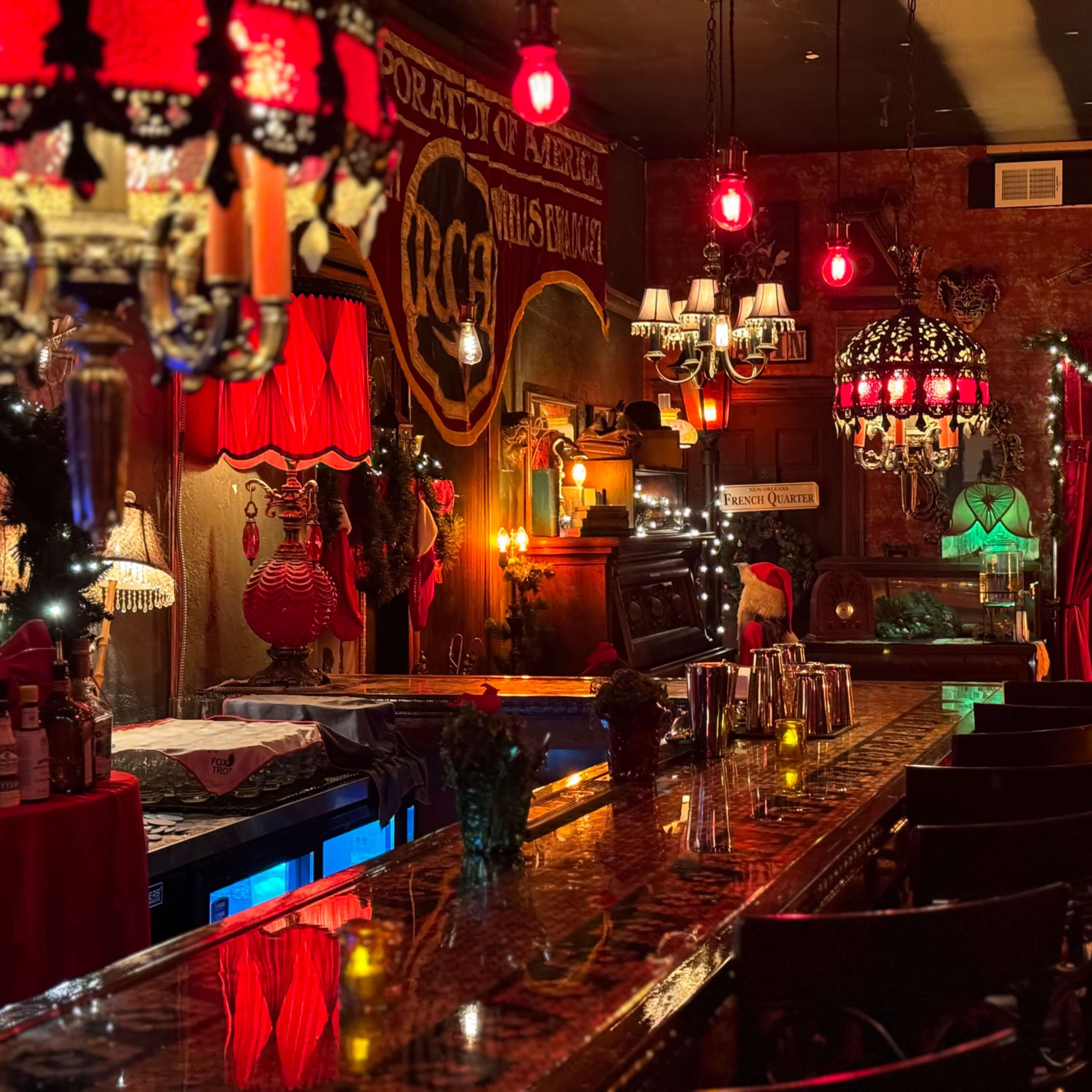 A dimly lit, vintage-style bar adorned with red lighting, chandeliers, and festive decorations.