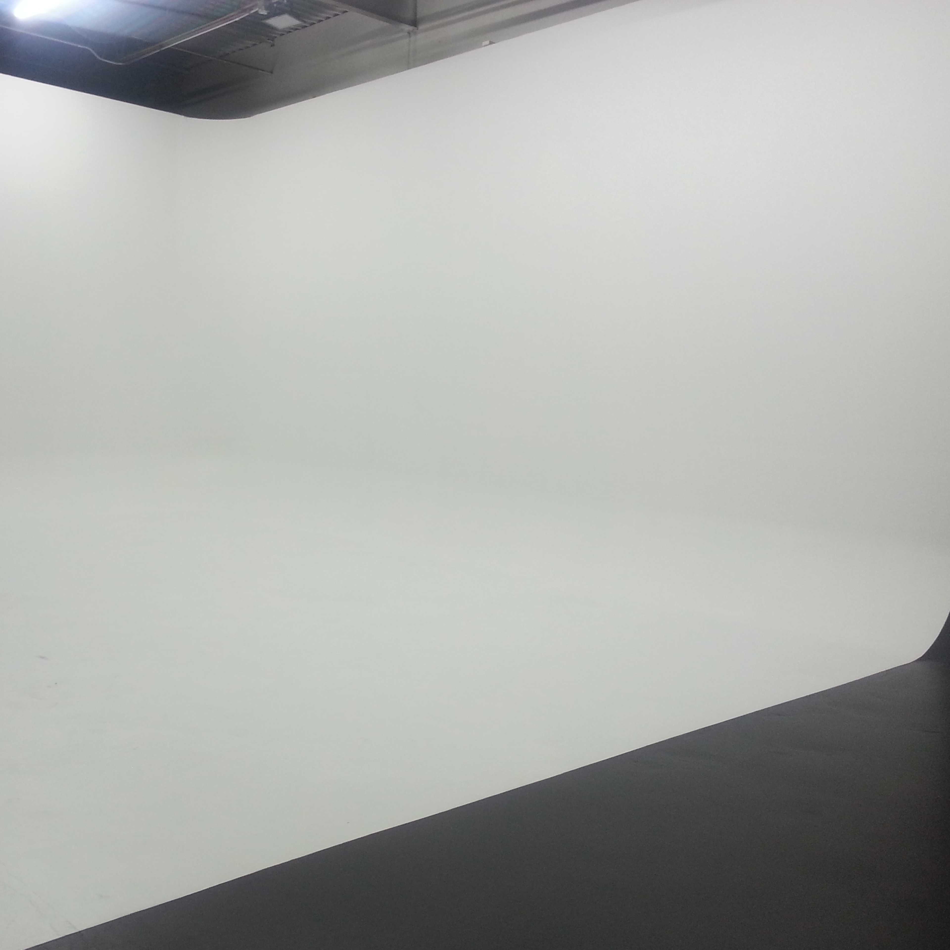 A photography studio with a seamless backdrop transitioning from a white surface to a black curve and a green background.